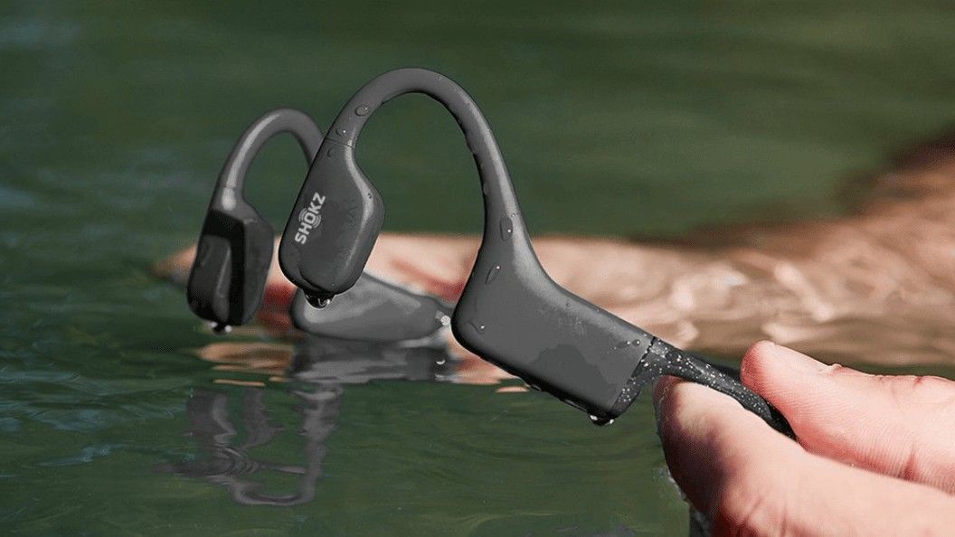Segurando os fones de ouvido de condução óssea Shokz na água