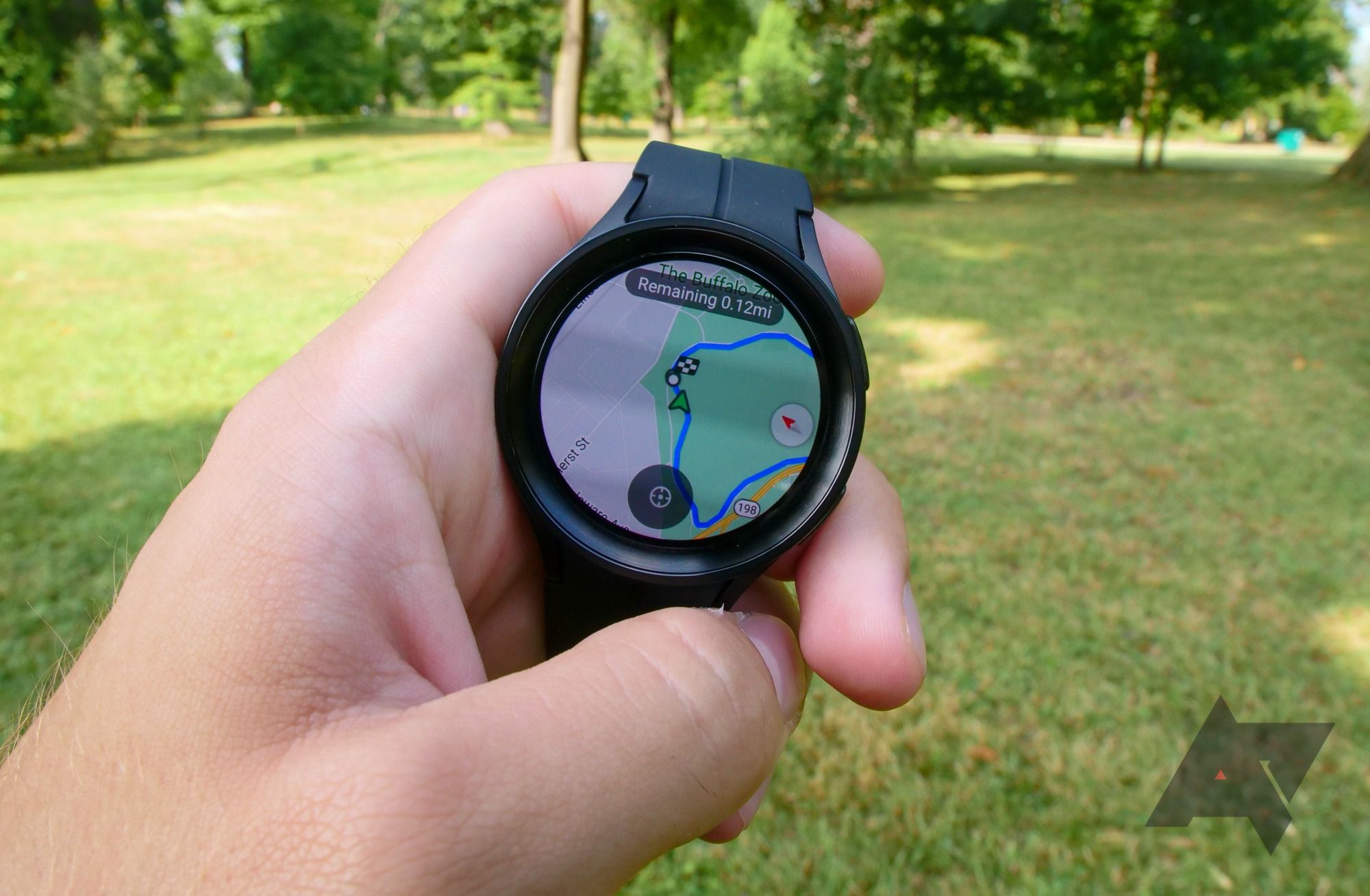 Uma mão segurando um Samsung Galaxy Watch 5 Pro com uma imagem desfocada de grama e árvores ao fundo