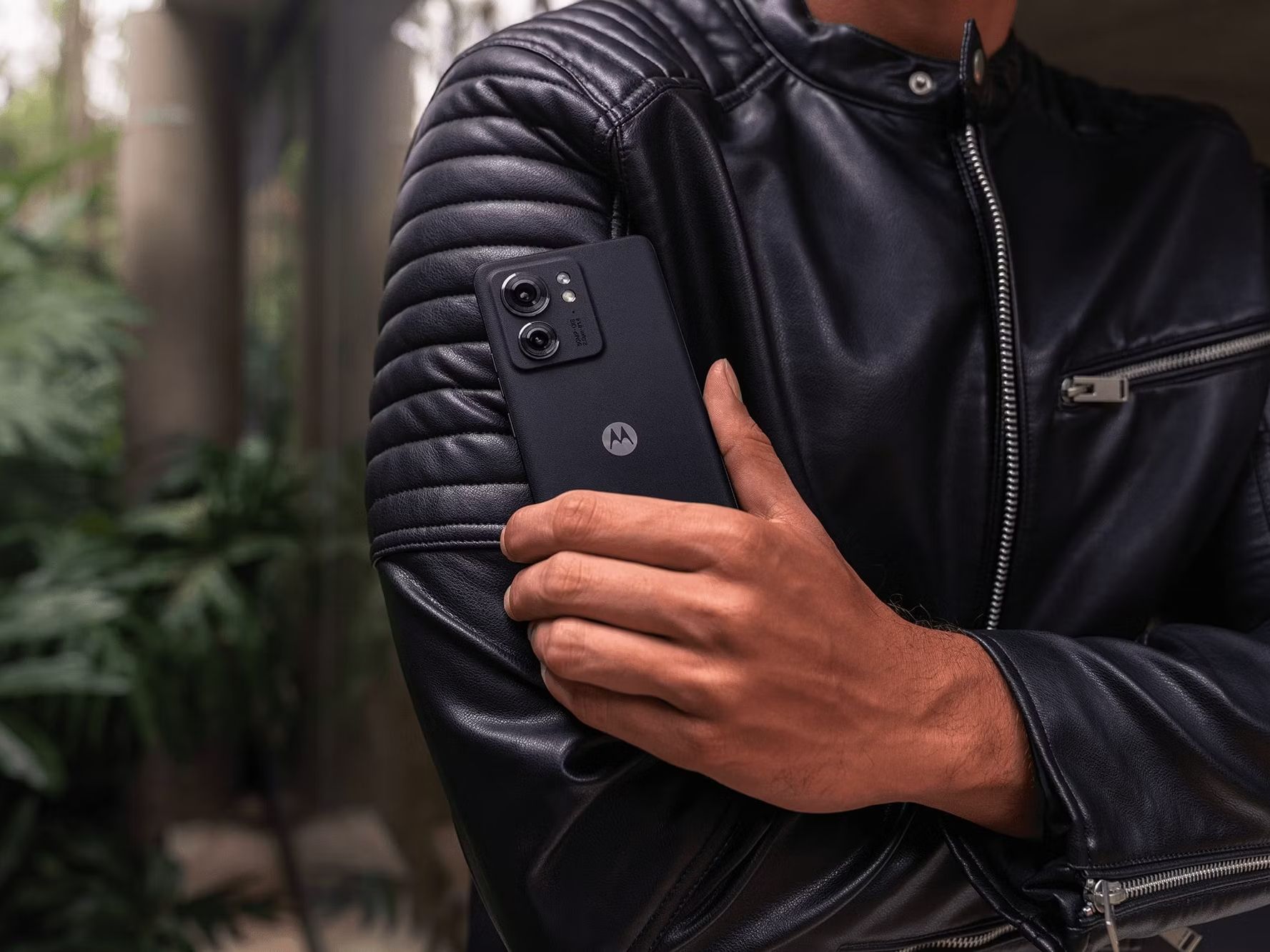 Um homem vestindo uma jaqueta de couro preta e segurando um telefone Motorola Edge (2023)