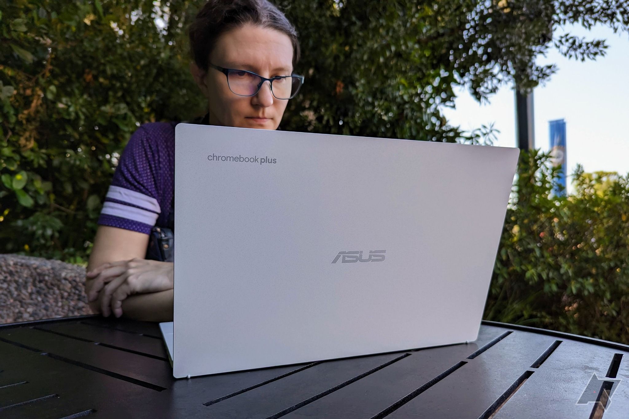 Um Asus Chromebook Plus CX34 sendo usado por uma pessoa sentada em uma mesa marrom do lado de fora