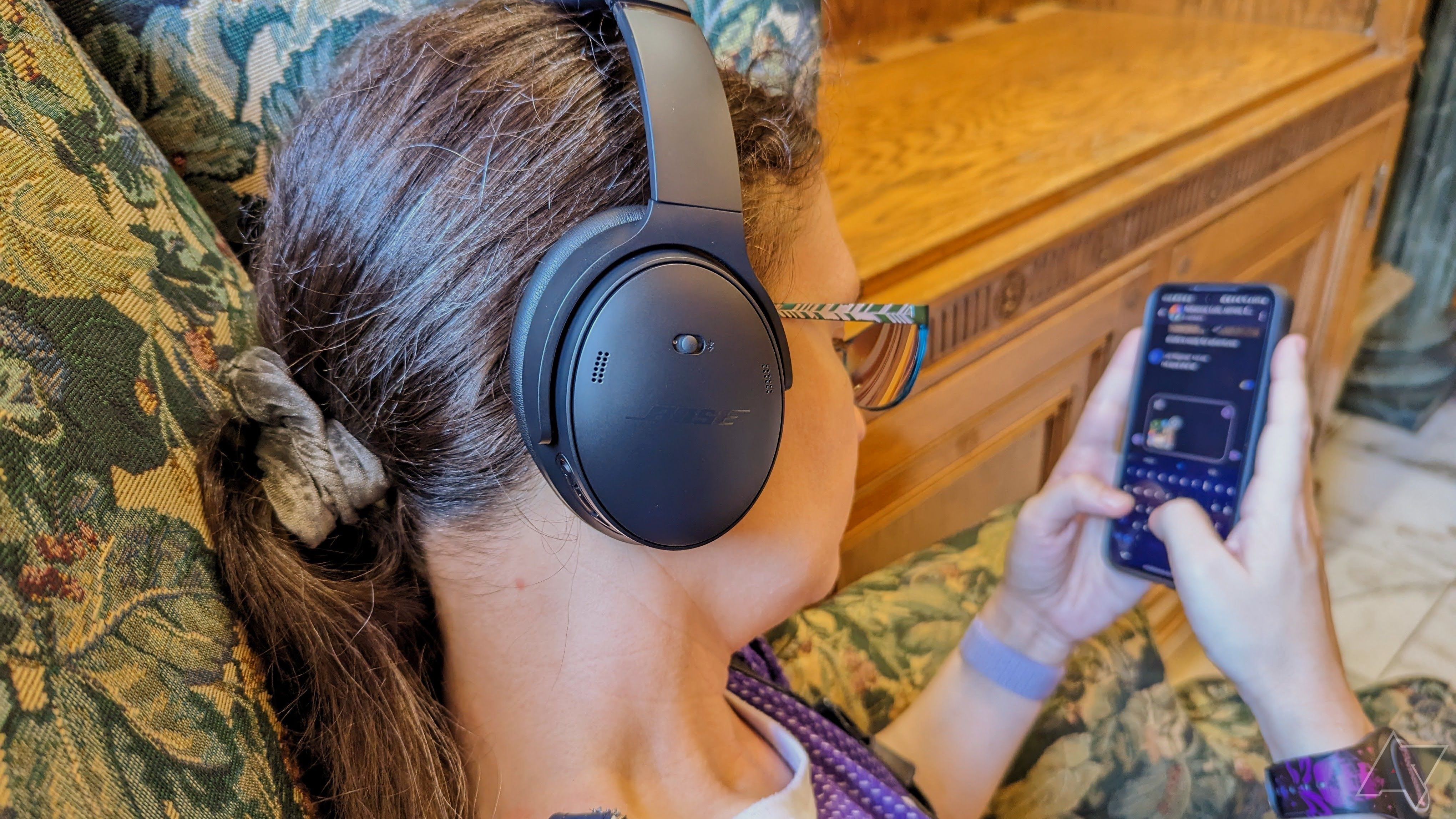Uma foto por cima do ombro de uma pessoa usando fones de ouvido e um smartphone.
