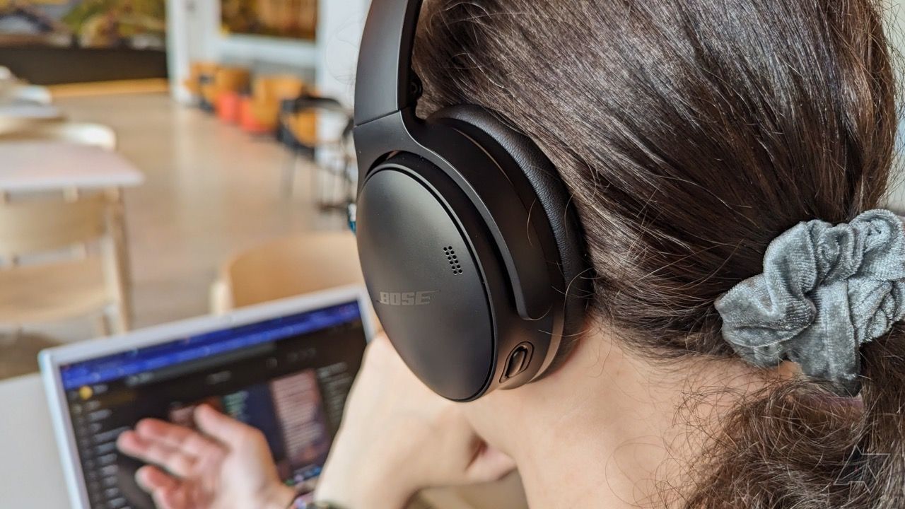 Foto por cima do ombro de alguém usando fones de ouvido e um laptop.