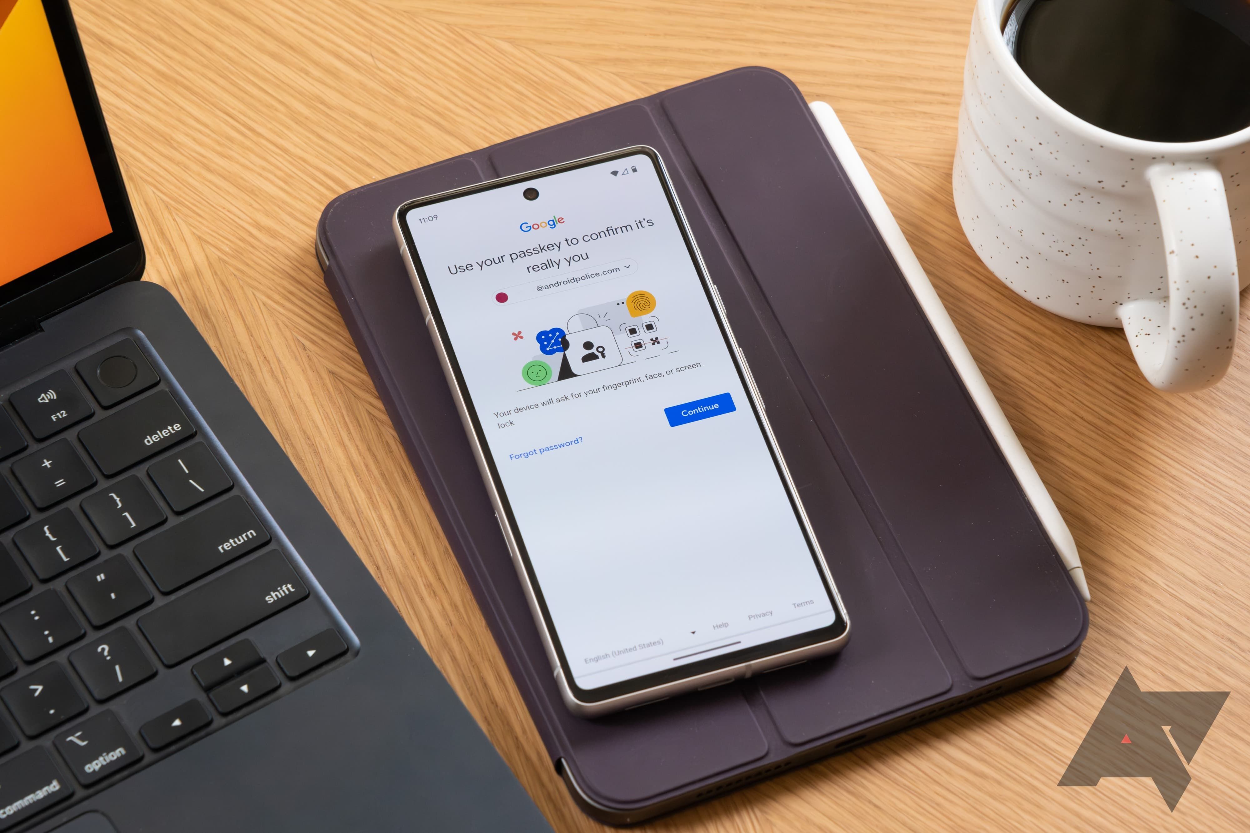 Um telefone com a tela de configuração do Google Passkey fica em uma capa de couro para tablet. Ele é ladeado por um laptop e uma caneca de café.