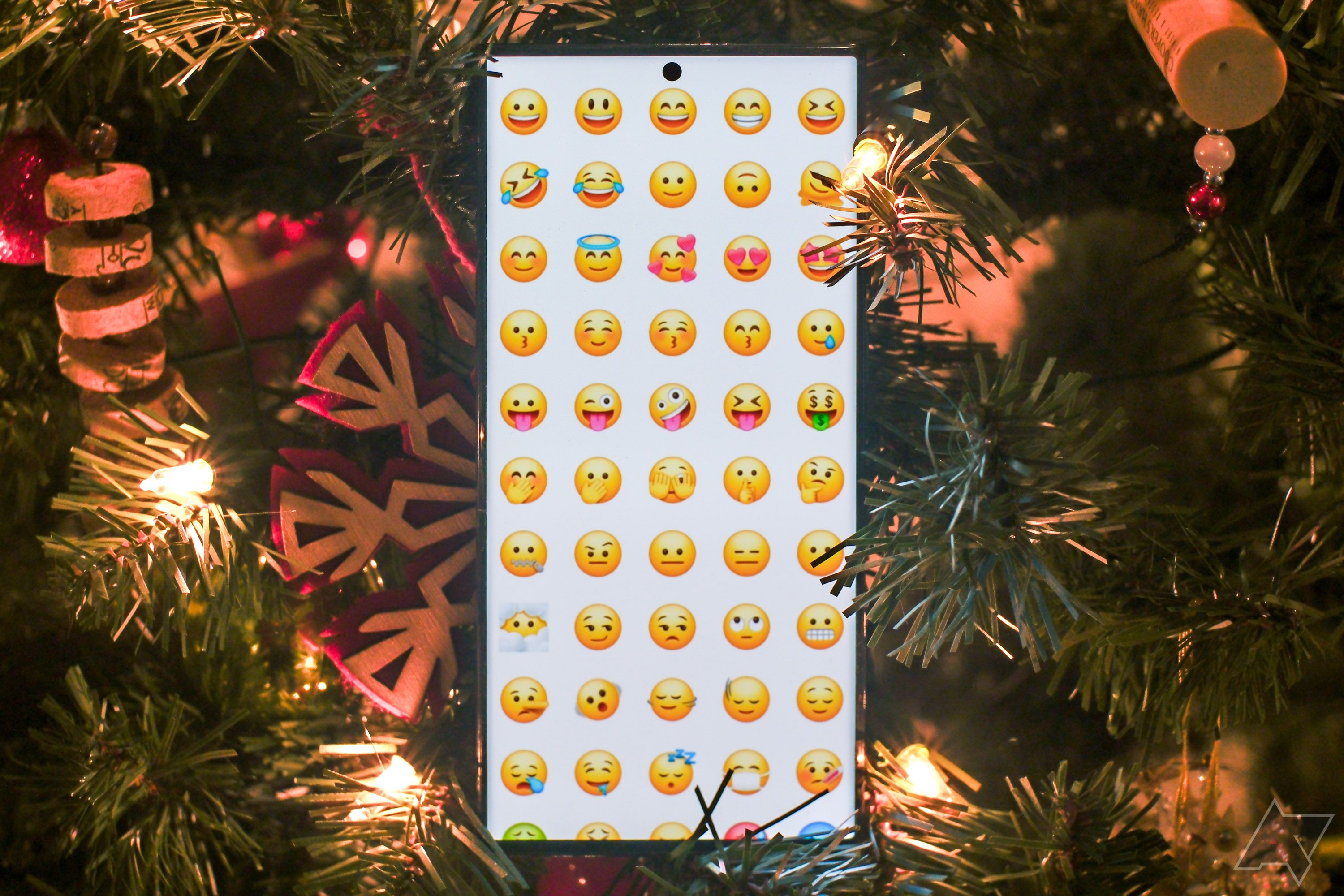 Um smartphone mostrando uma grade de emojis cercados por decorações natalinas