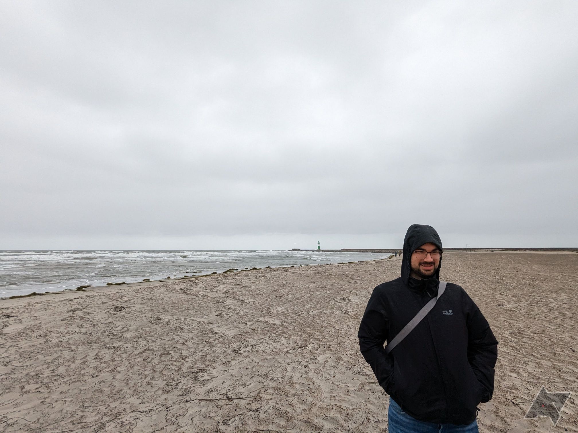 homem com capa de chuva preta em pé na praia sob céu nublado