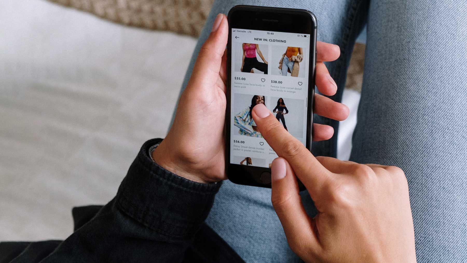 Uma pessoa de suéter preto e jeans acessa um aplicativo de compras em seu telefone. 