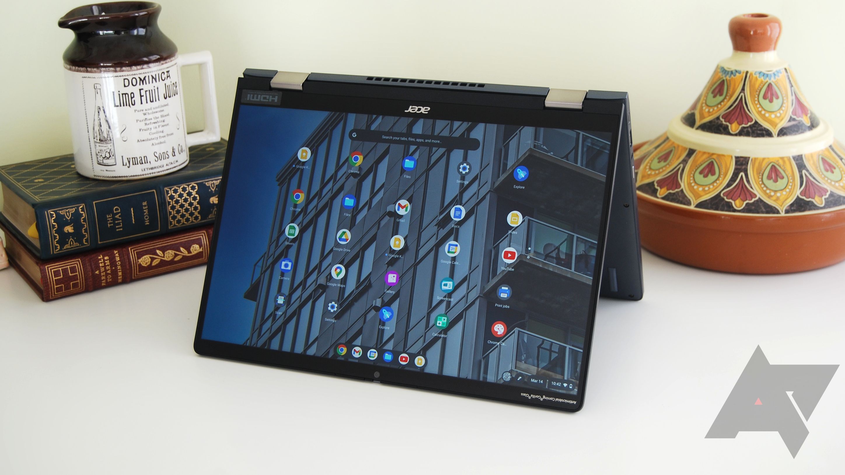 Um Acer Chromebook Spin 714 em modo tenda em uma mesa branca com livros, uma caneca e um pedaço de cerâmica ao fundo