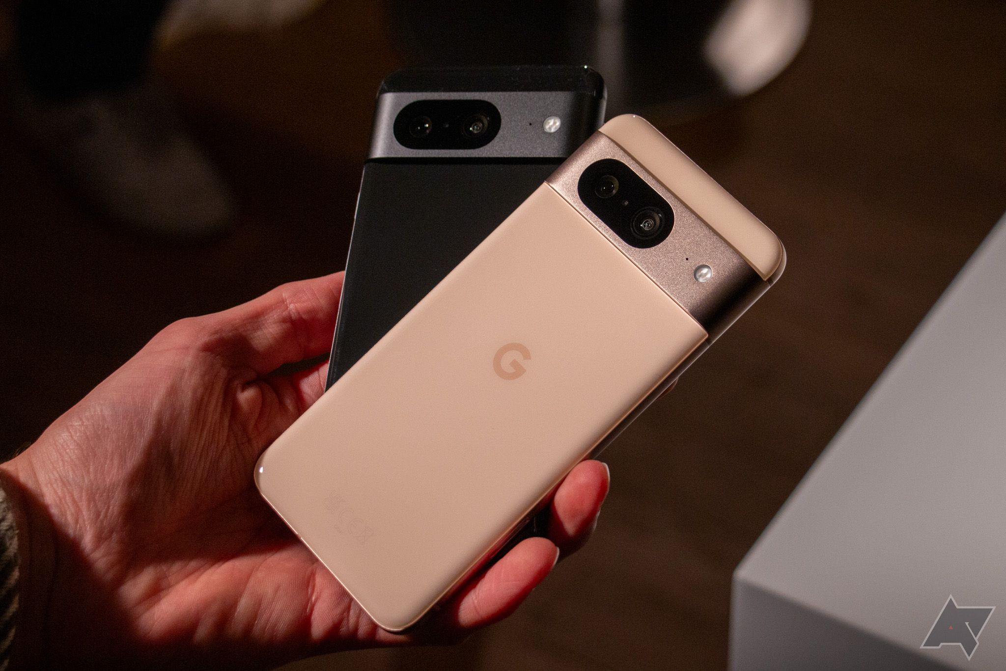 Uma mão segurando dois smartphones Google Pixel 8, um preto e outro rosa peônia.