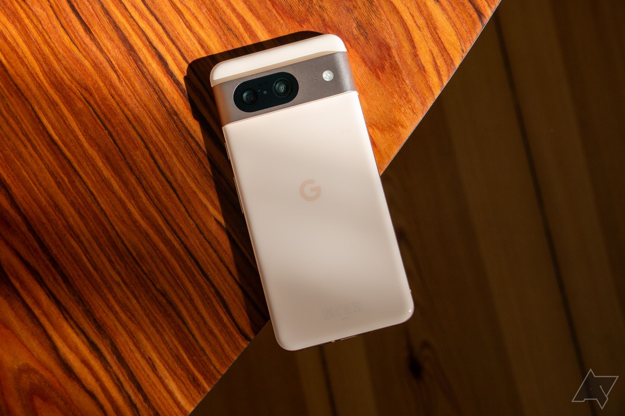 Um Google Pixel 8 branco virado para baixo sobre uma mesa de madeira marrom.