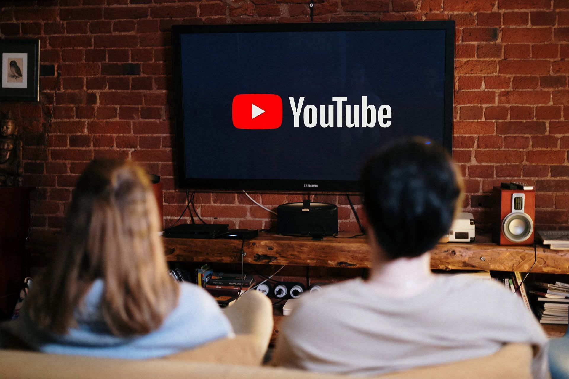 Duas pessoas estão olhando para uma televisão com o logotipo do YouTube exibido. 
