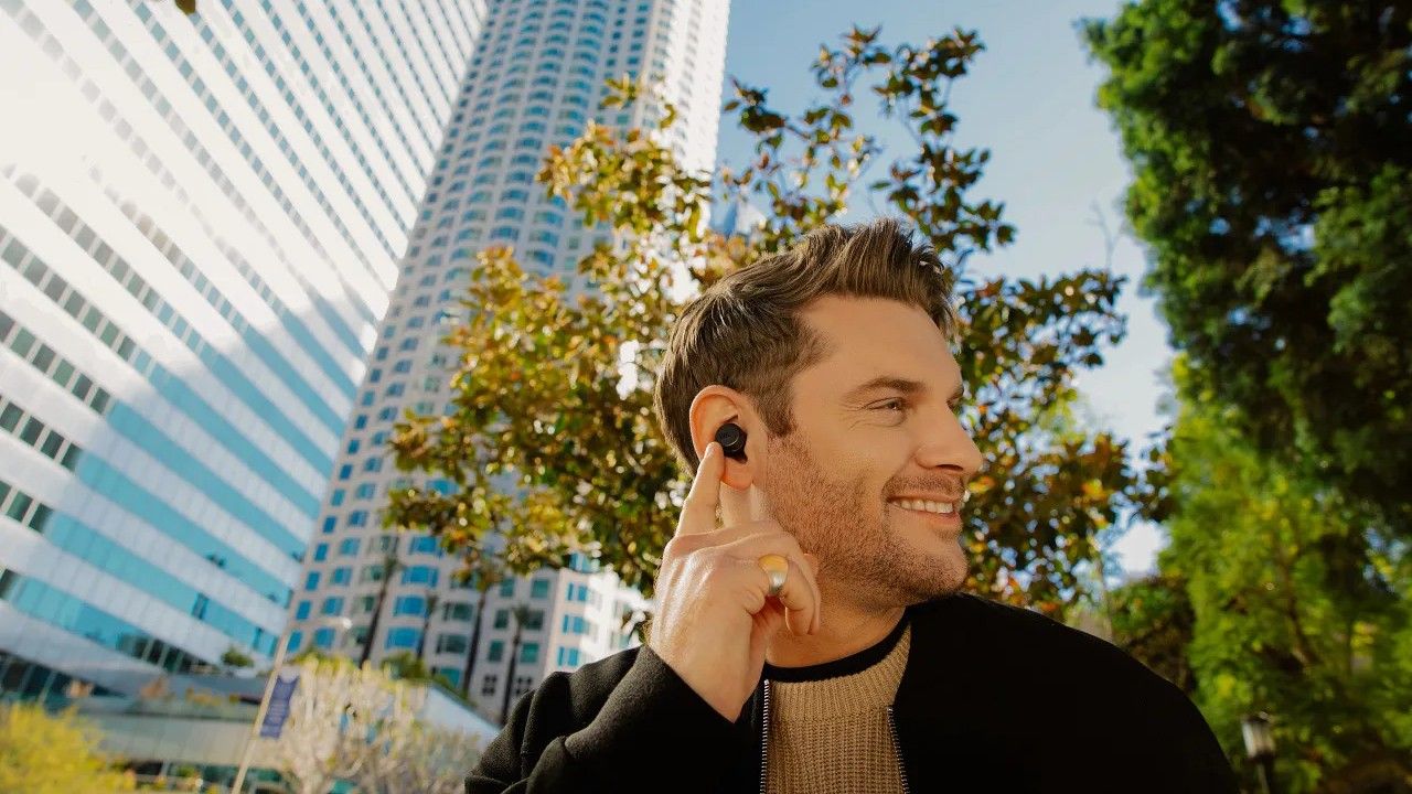 Uma pessoa usando os fones de ouvido JBL Tour Pro+ e apontando para eles contra um fundo externo