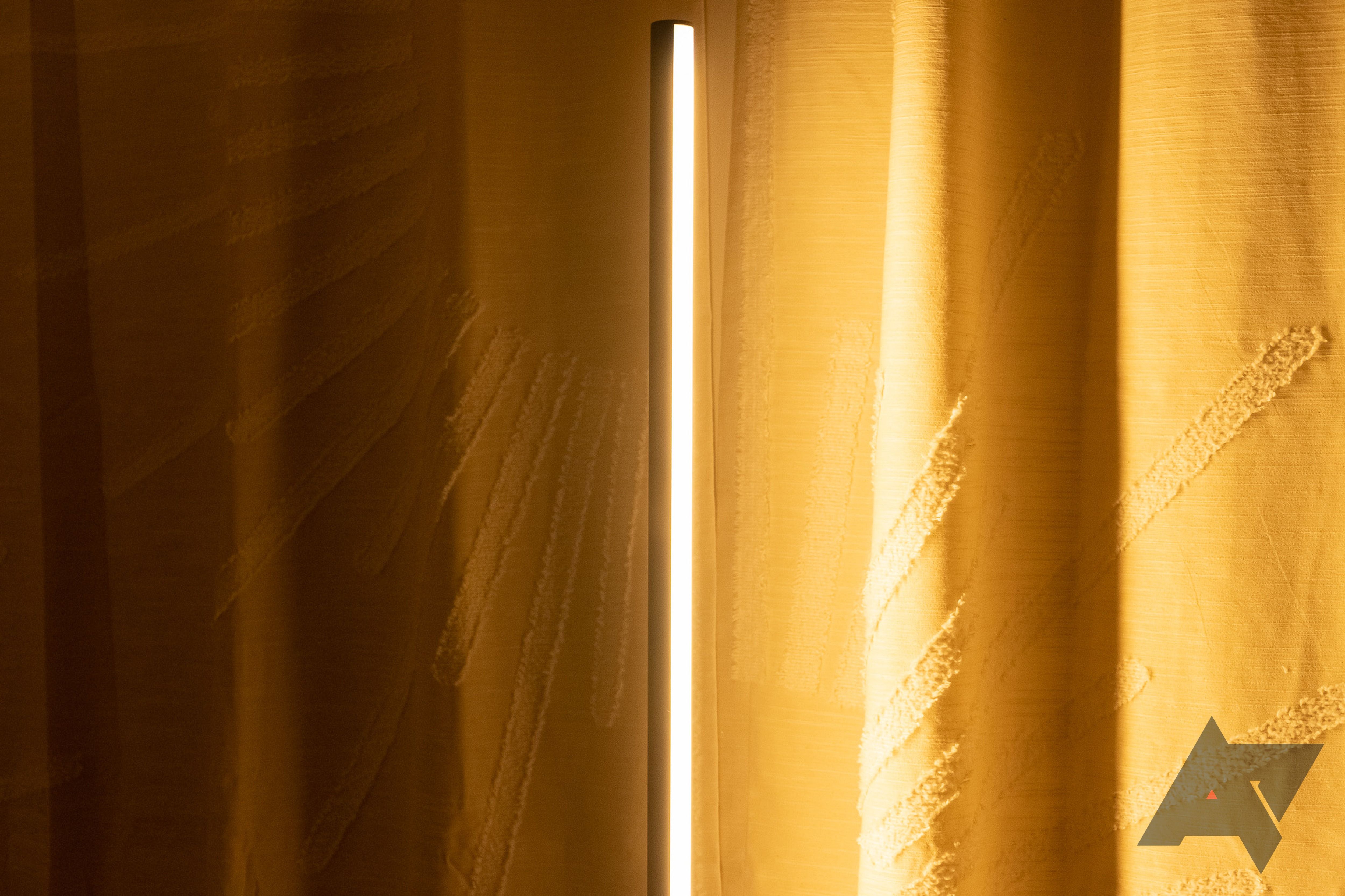 Uma luminária de chão Philips Hue Signe contra uma cortina amarela.