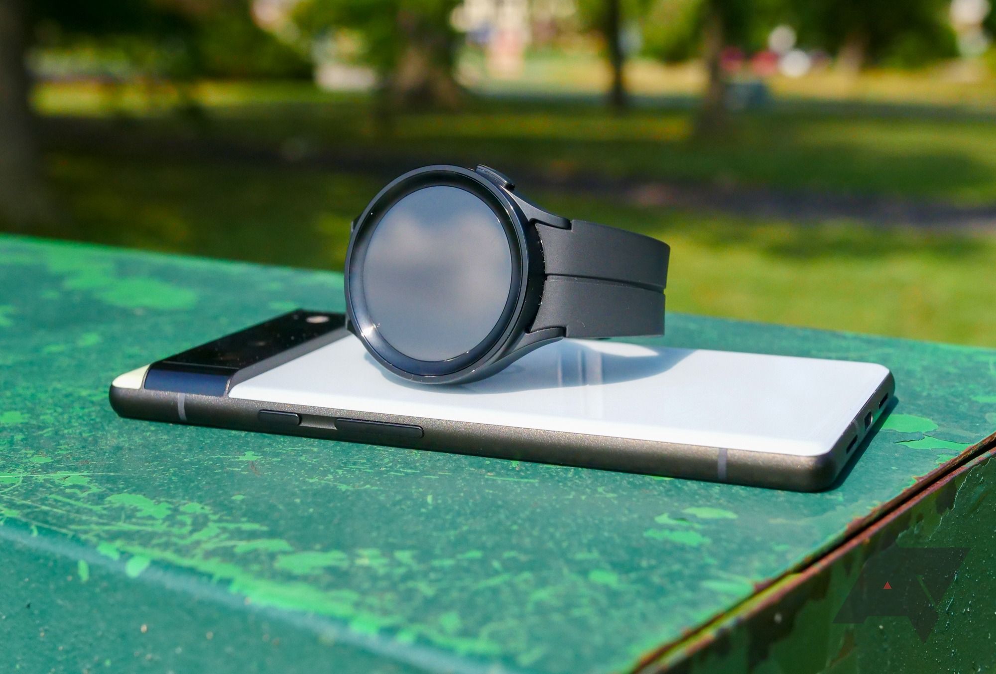 Um smartwatch em cima de um smartphone em uma mesa em um parque.
