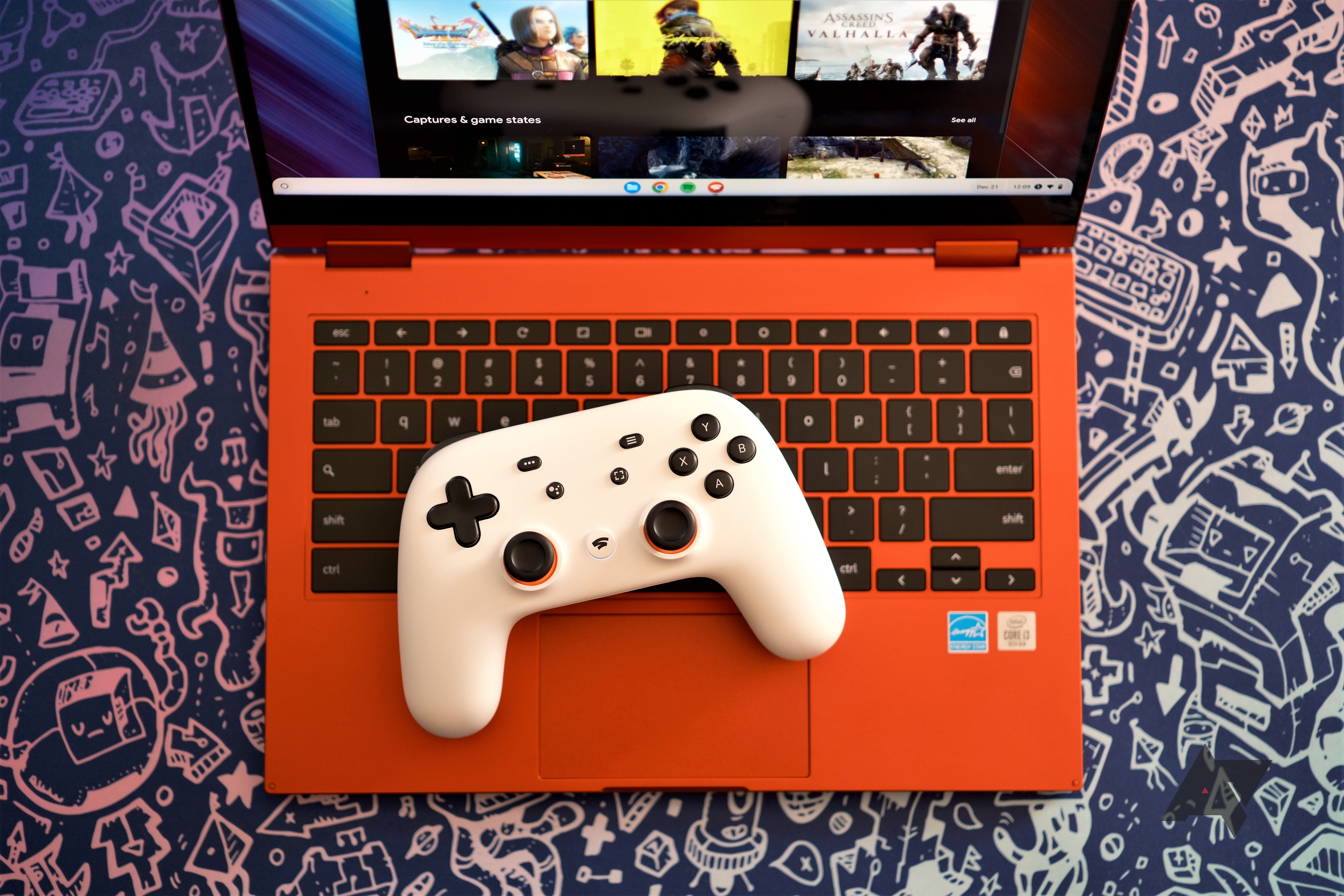 Um controlador branco do Google Stadia no teclado de um Chromebook vermelho com um serviço de jogos aberto na tela.  O laptop está sobre um fundo azul com gráficos prateados de imagens de videogame.