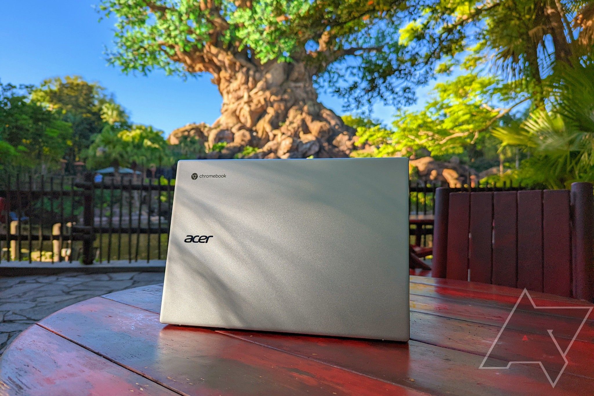 Um Acer Chromebook 514 (CB514-2H/T) sobre uma mesa de madeira em um pátio de pedra ao lado de um lago com vegetação ao redor