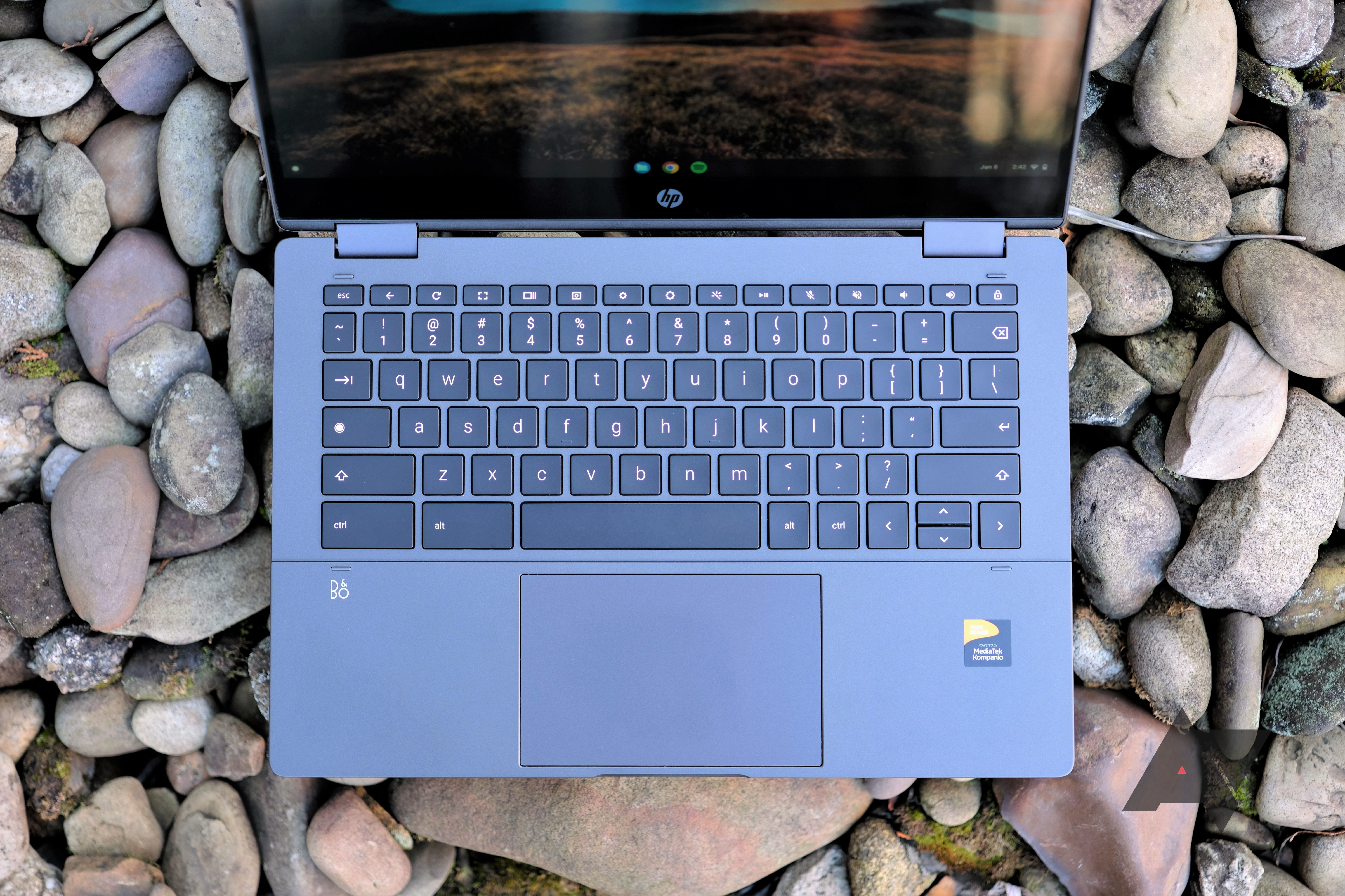 Um Chromebook HP x360 13b em cima de uma cama de pedras com o teclado e o trackpad à vista