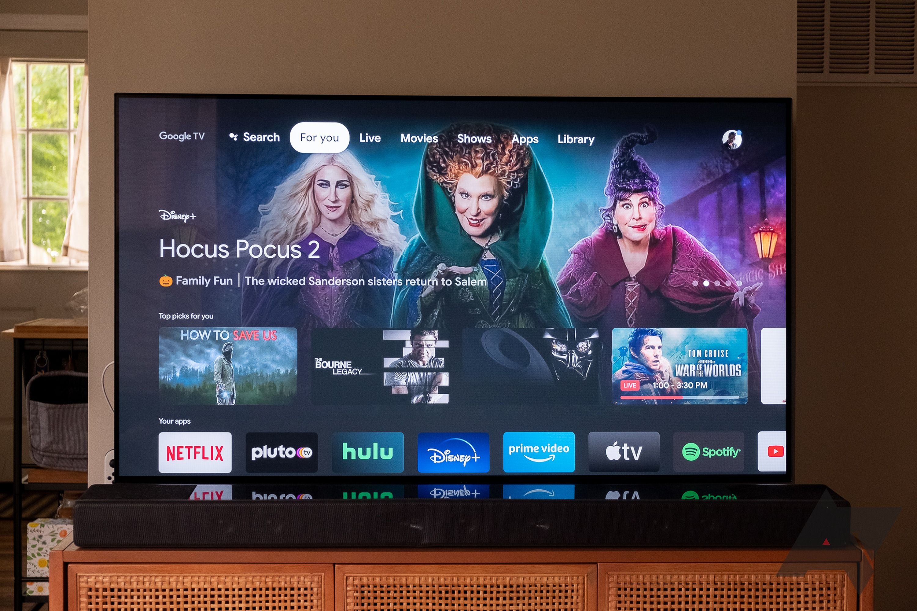 Uma TV grande em um suporte em uma casa com a tela inicial do Google TV exibida.