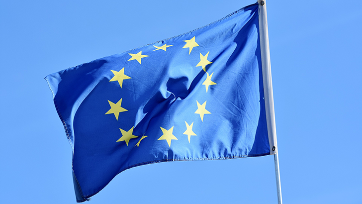 A bandeira da União Europeia contra um fundo azul tremulando ao vento.