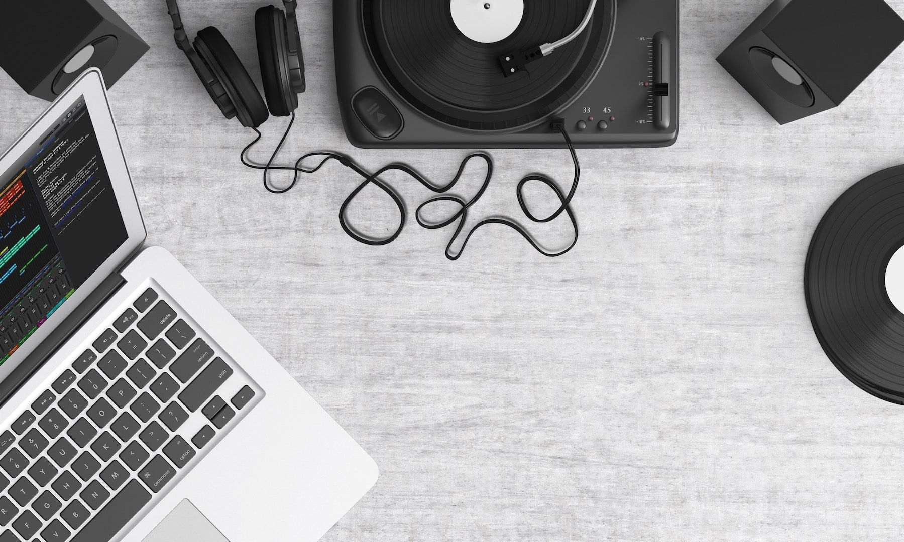 Um laptop, um toca-discos e fones de ouvido estão sobre uma mesa cinza.