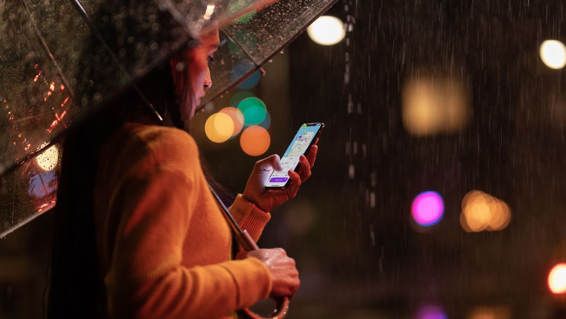 Uma mulher usa um iPhone com um guarda-chuva transparente na chuva em uma rua escura.