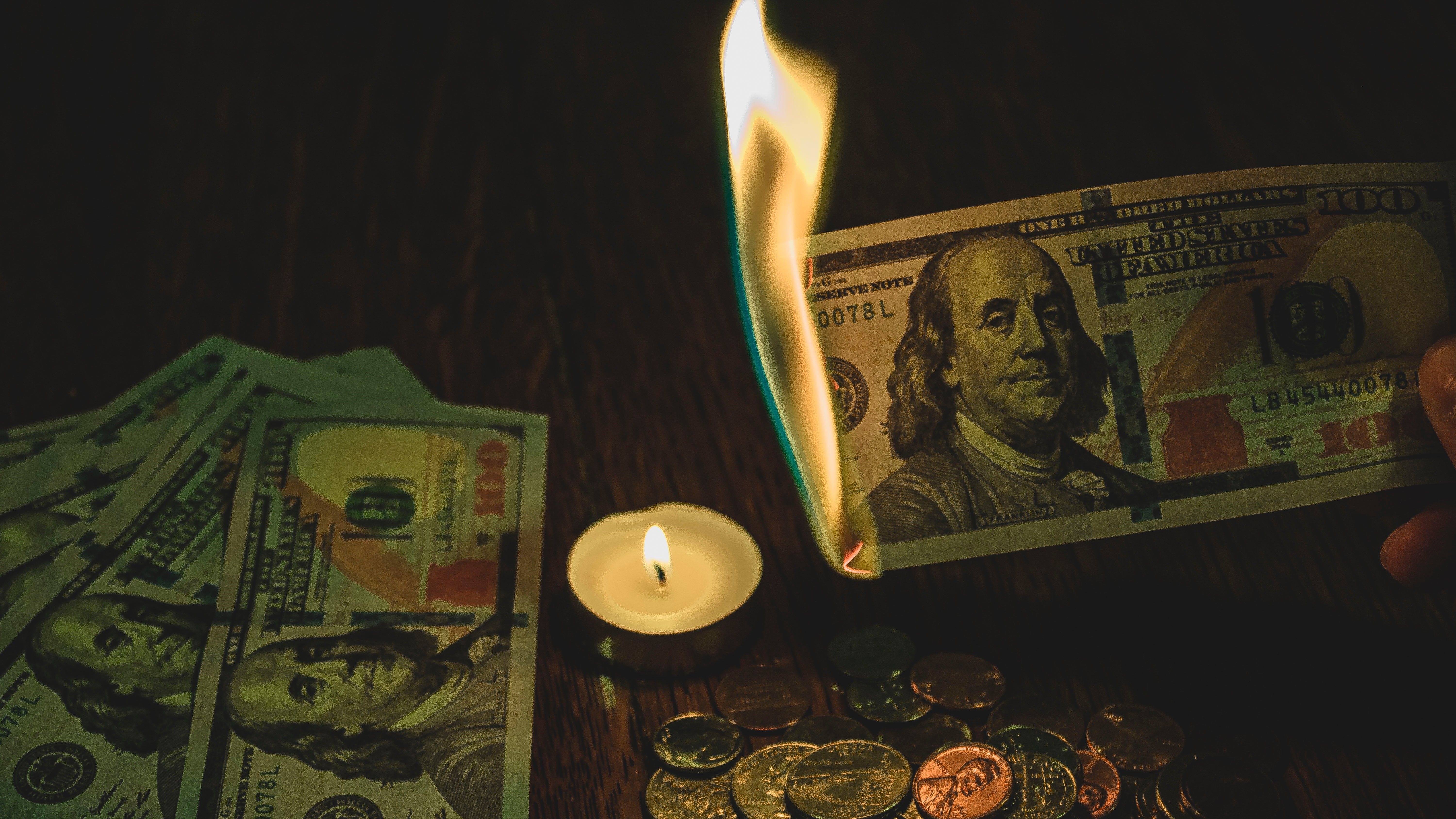 Papel-moeda segurado sobre a chama de uma vela acesa no fogo.