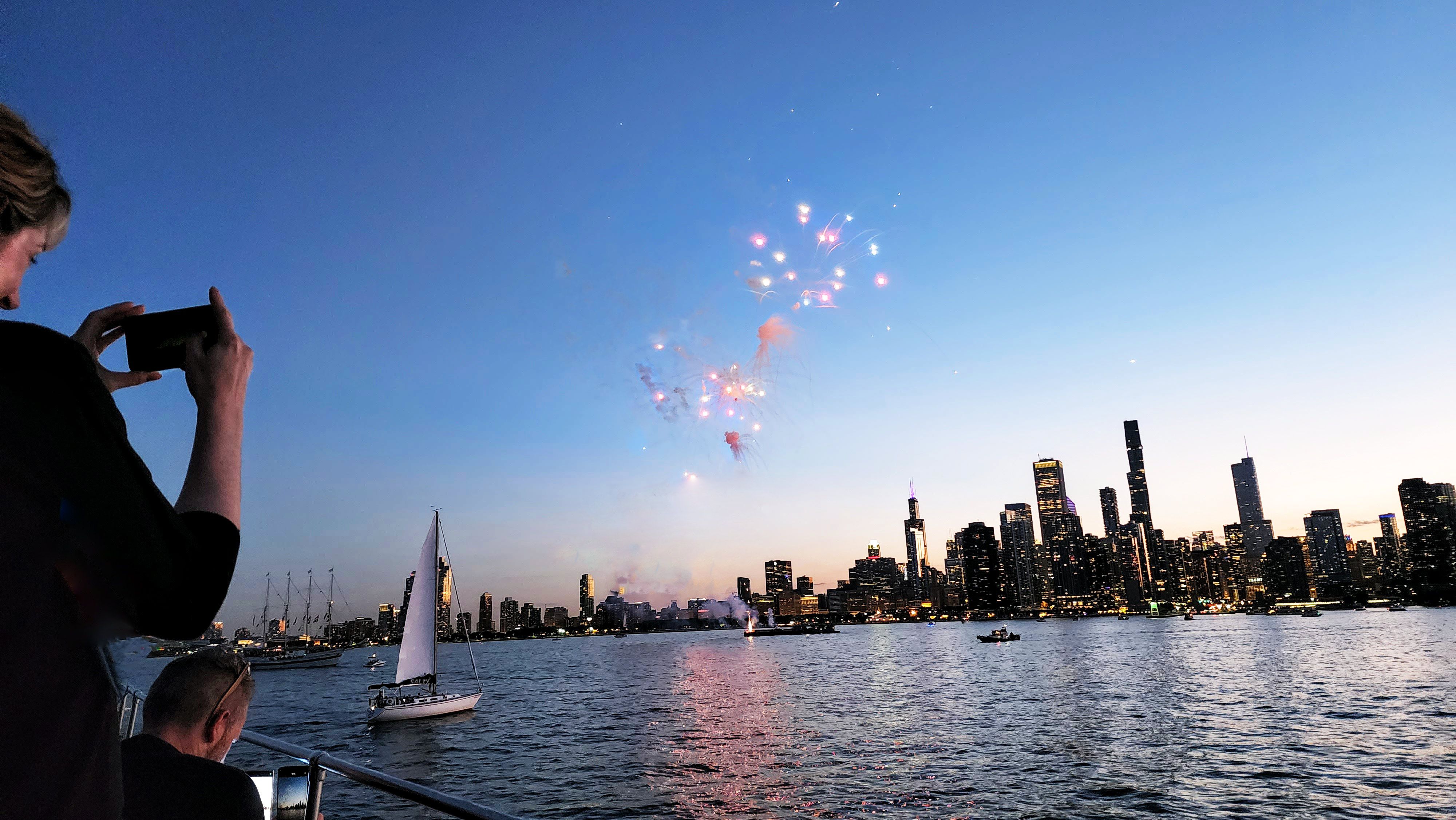 Duas pessoas em um barco usando seus smartphones para tirar fotos de fogos de artifício no horizonte de Chicago. 