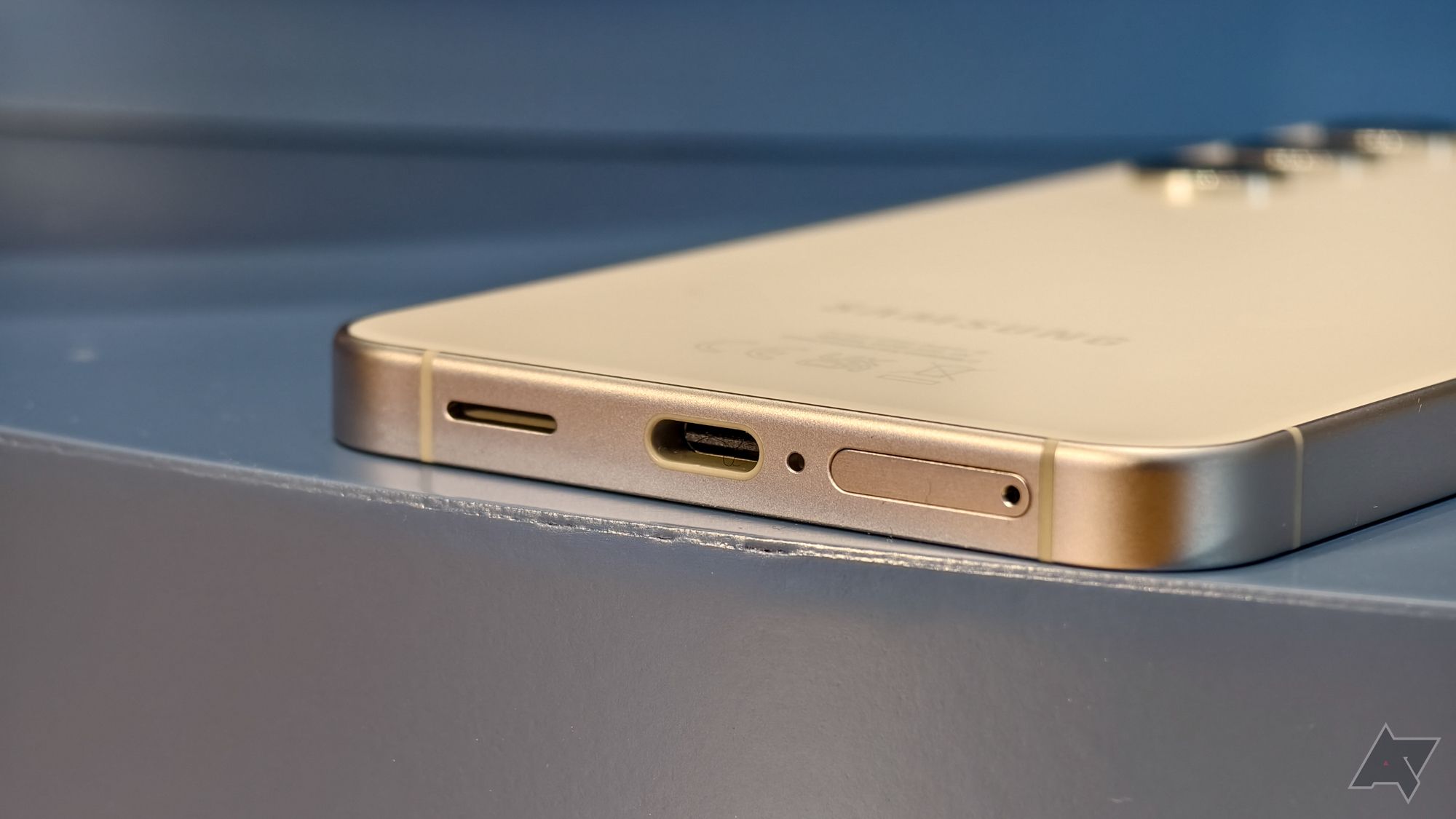 Samsung Galaxy S24 na cor branca, apoiado sobre uma mesa, mostrando a porta USB-C
