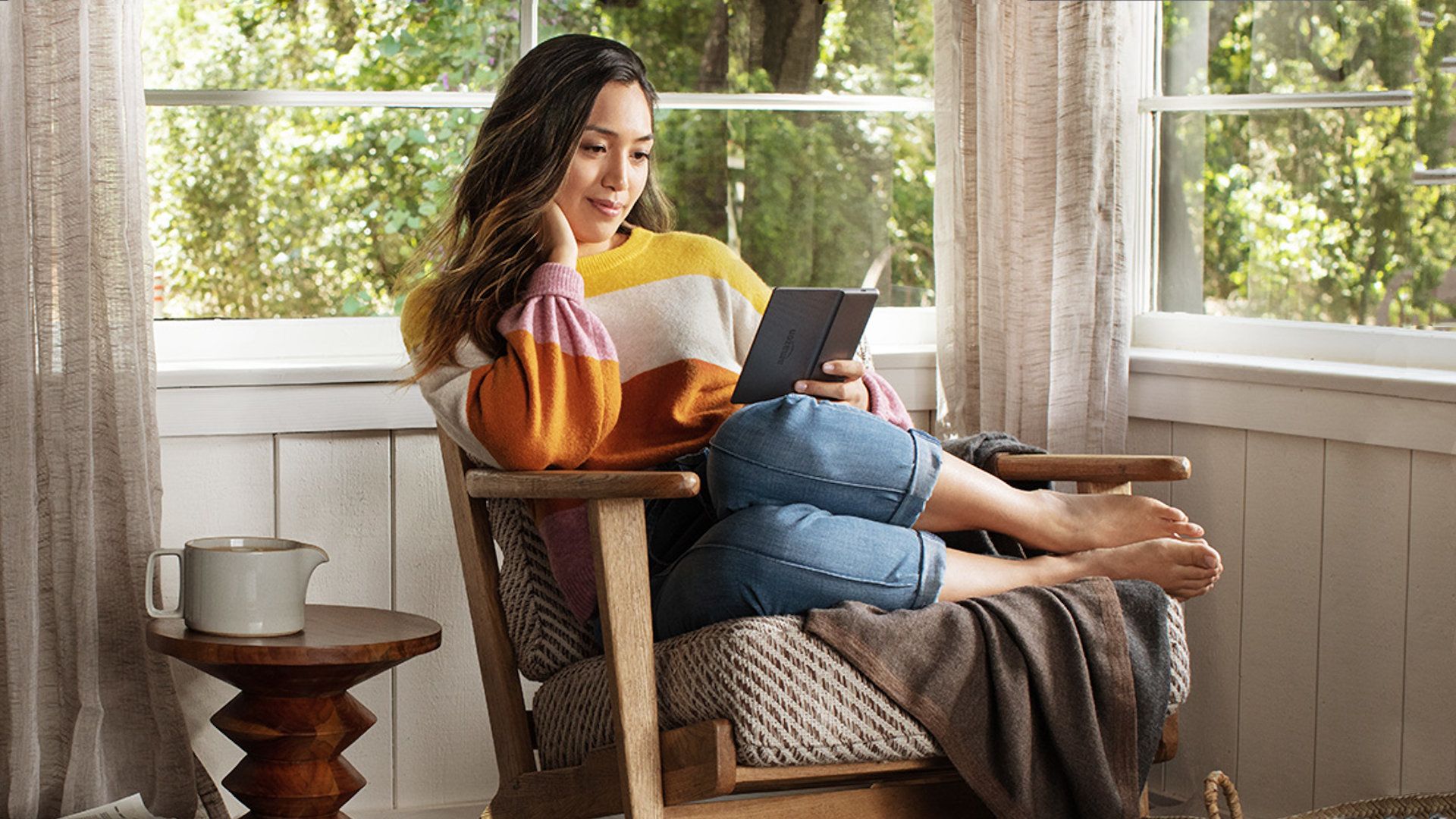 Uma modelo sentada de lado em uma cadeira lendo com um Kindle Oasis.
