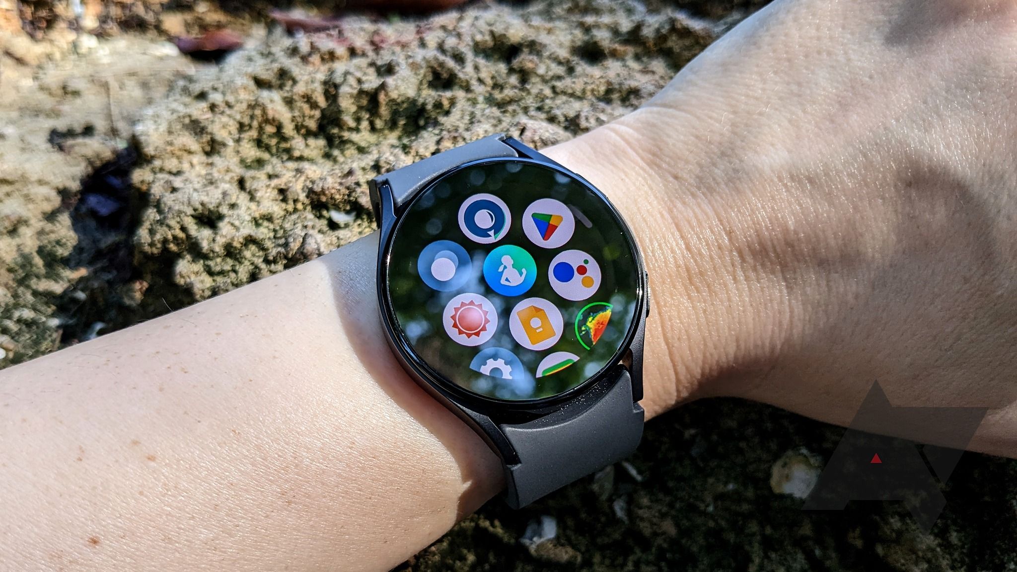 Galaxy Watch 5 sendo usado no pulso em frente a um fundo rochoso com a tela da gaveta de aplicativos ligada