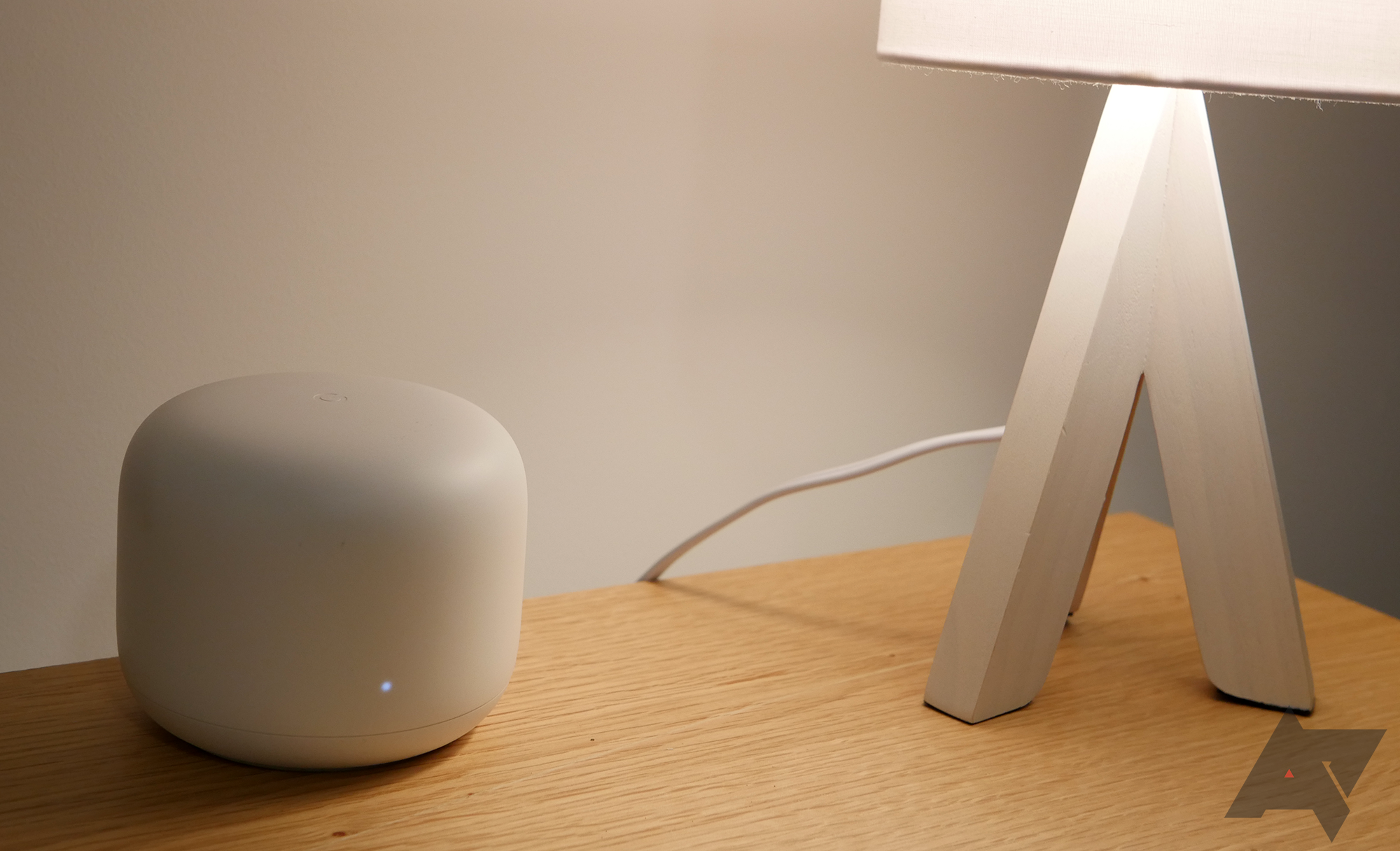 Um roteador Google Nest Wifi sobre uma mesa de madeira com uma luminária.