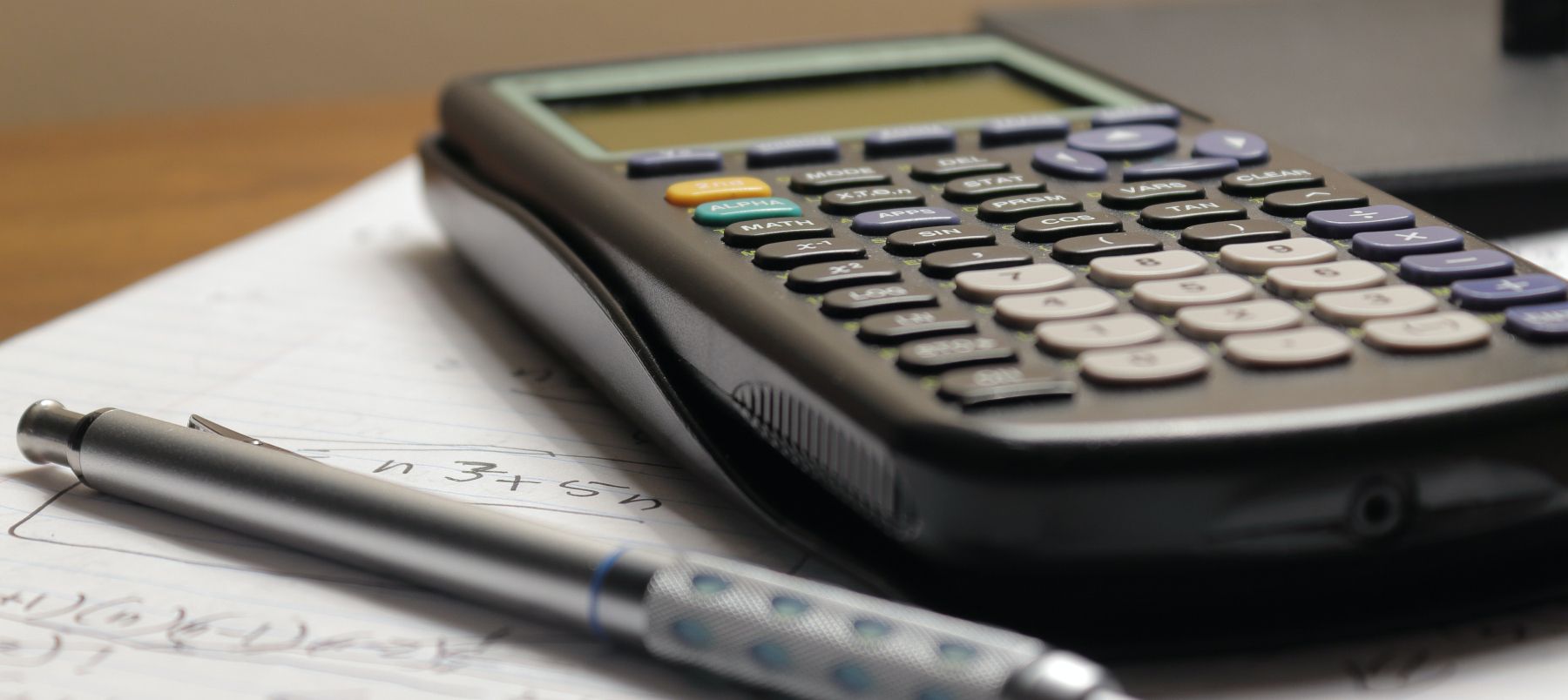 Uma calculadora e uma caneta colocadas em um bloco de notas com equações matemáticas escritas nele