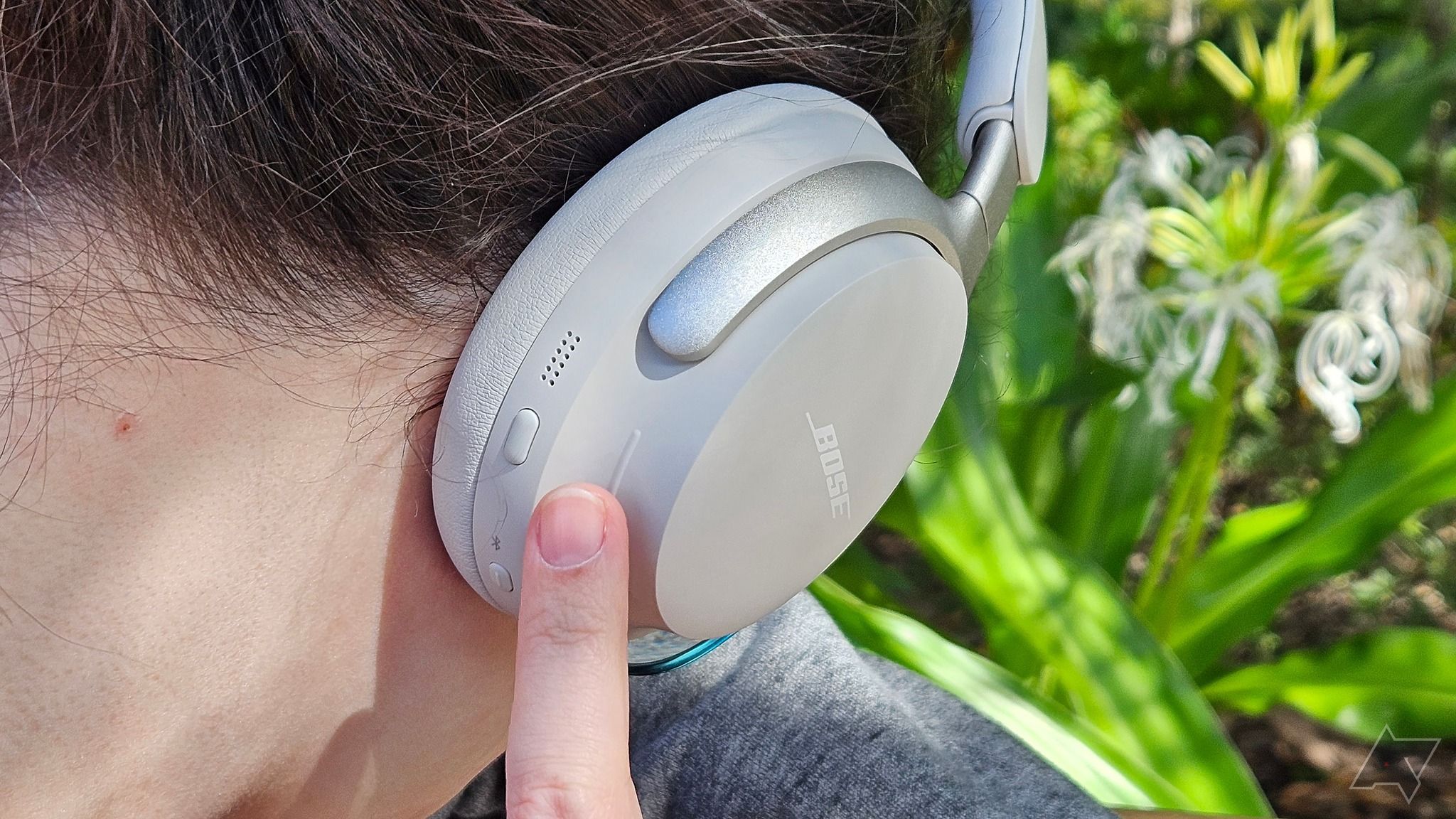 O lado direito dos fones de ouvido Bose QuietComfort Ultra com um dedo ajustando o volume.