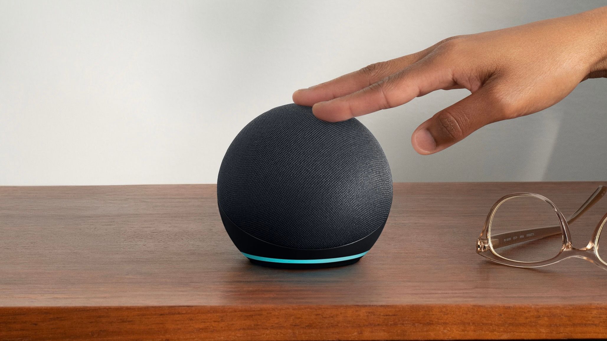 Mão tocando Amazon Echo Dot em uma mesa de madeira.