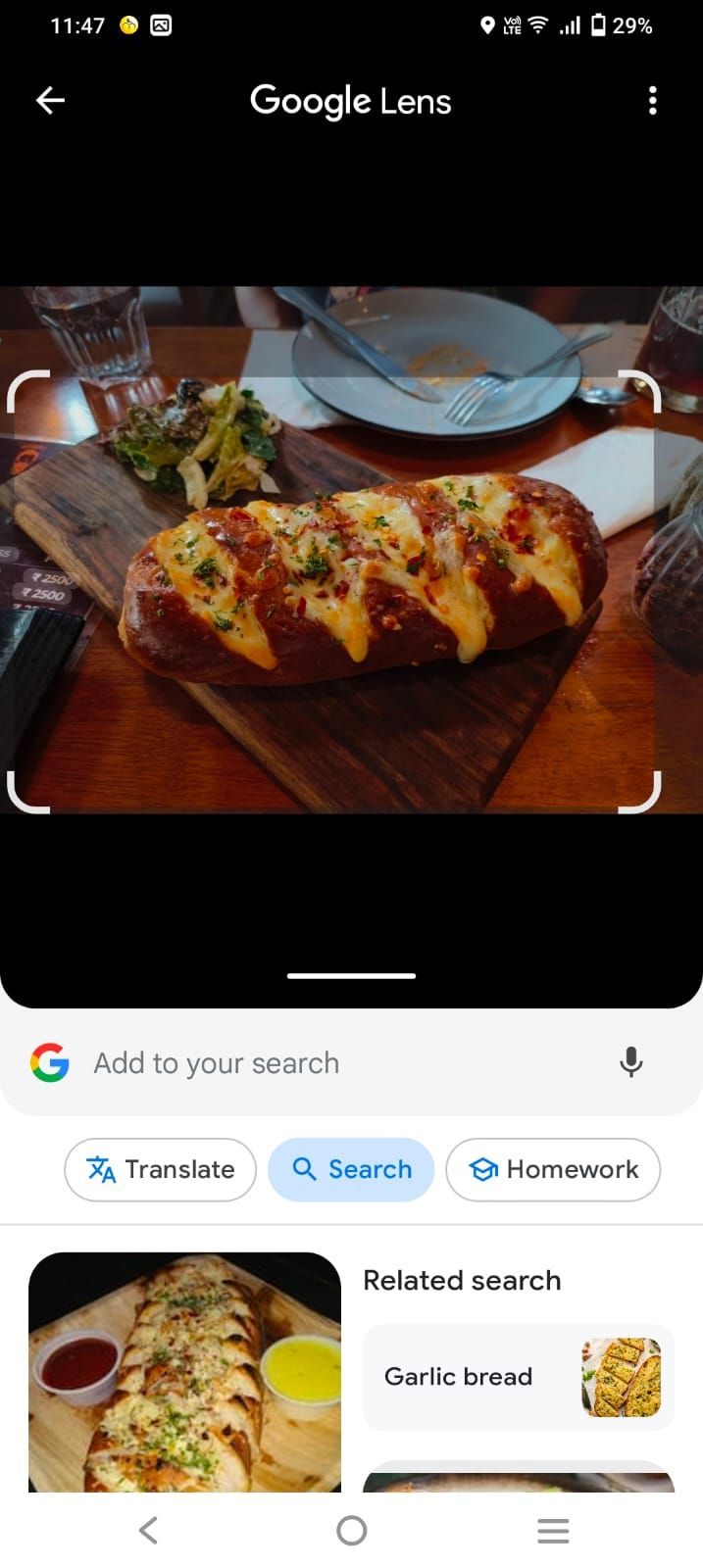 A imagem mostra a pesquisa do Google Lens após selecionar uma foto salva de pão de alho.  Os resultados da pesquisa relacionada são mostrados na parte inferior da tela.