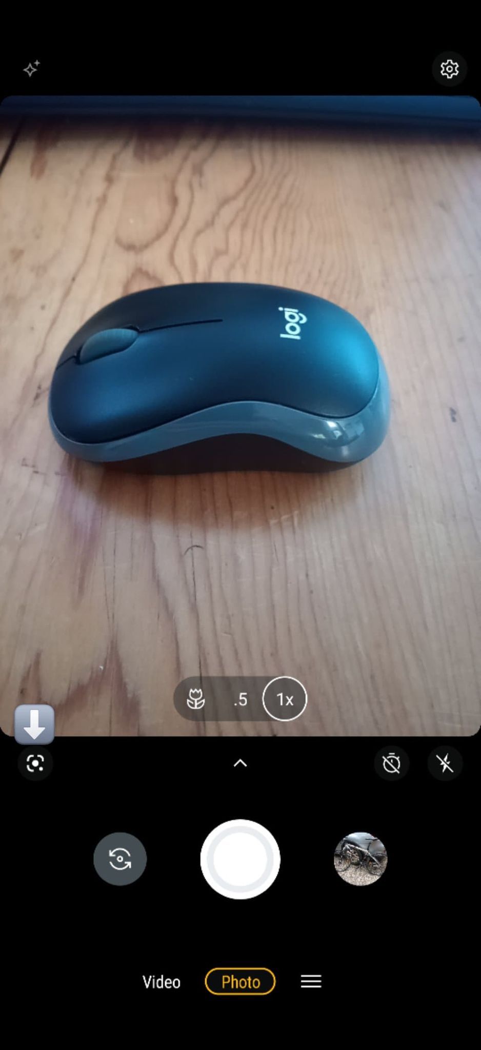 A imagem mostra o aplicativo da câmera Android aberto com um mouse de computador na tela e uma seta apontando para o ícone do Google Lens no canto inferior esquerdo.