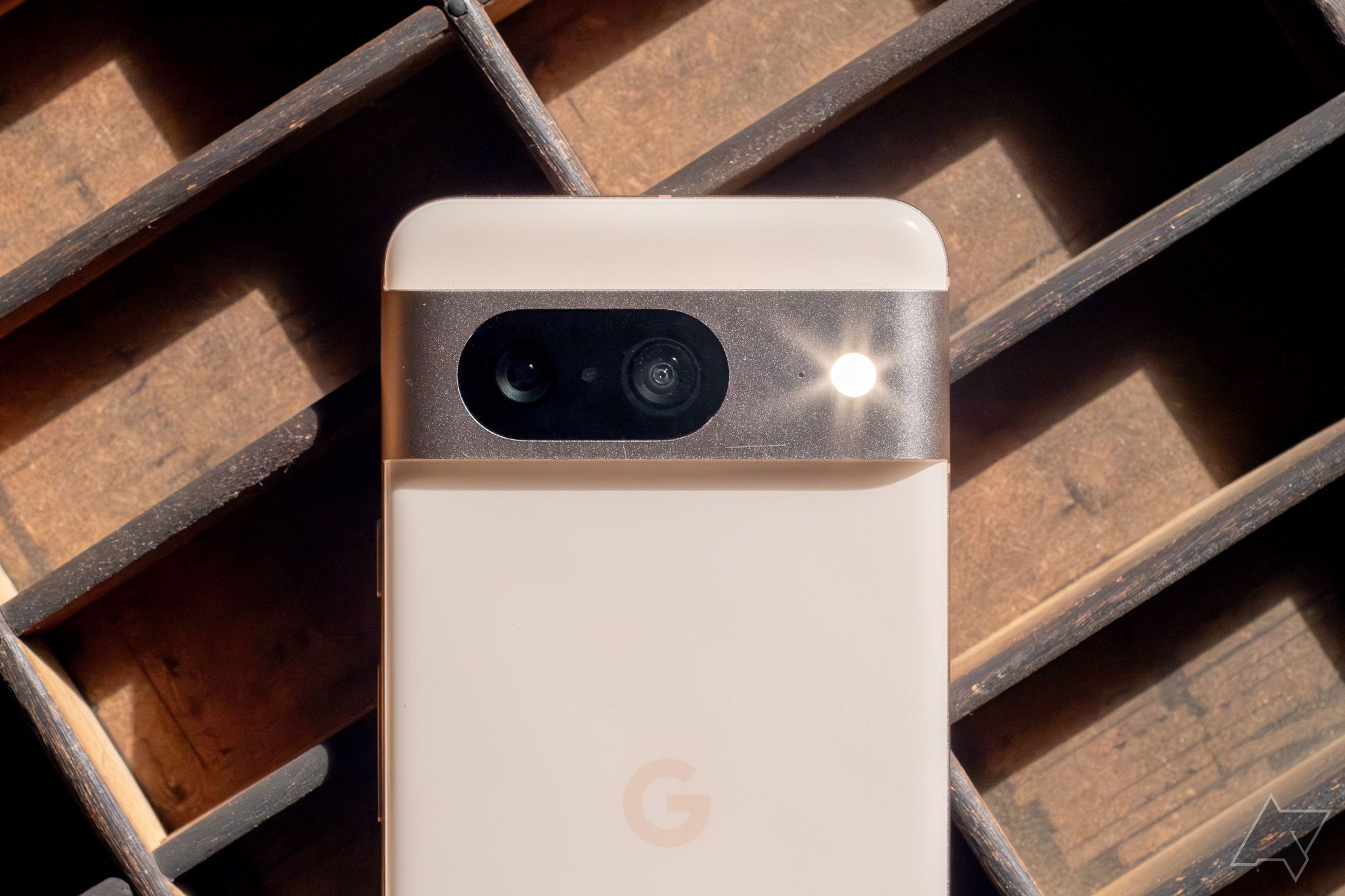 Um smartphone Google rosa, virado para baixo e com o flash da câmera ligado, em uma grade de madeira.