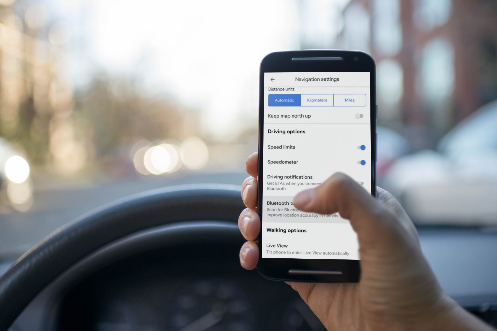 Uma mão segurando um telefone em um carro com uma captura de tela da página de configurações do Google Maps exibida no telefone