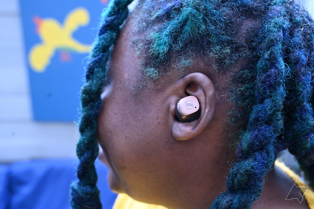 Vista lateral de uma mulher afro-americana usando fones de ouvido Sennheiser Momentum True Wireless 4 com lotes coloridos