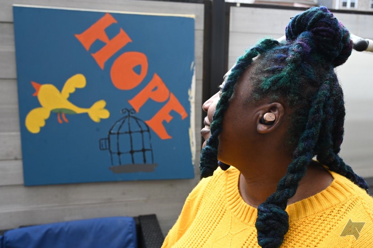 Mulher afro-americana usando fones de ouvido Sennheiser Momentum True Wireless 4 olhando para a pintura de um pássaro voando livre com a palavra esperança.