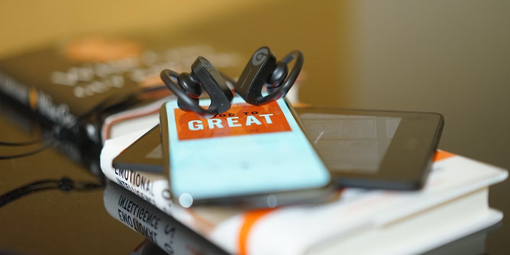 dois fones de ouvido pretos apoiados em um telefone que está em um Kindle que está em um livro que está sobre uma mesa