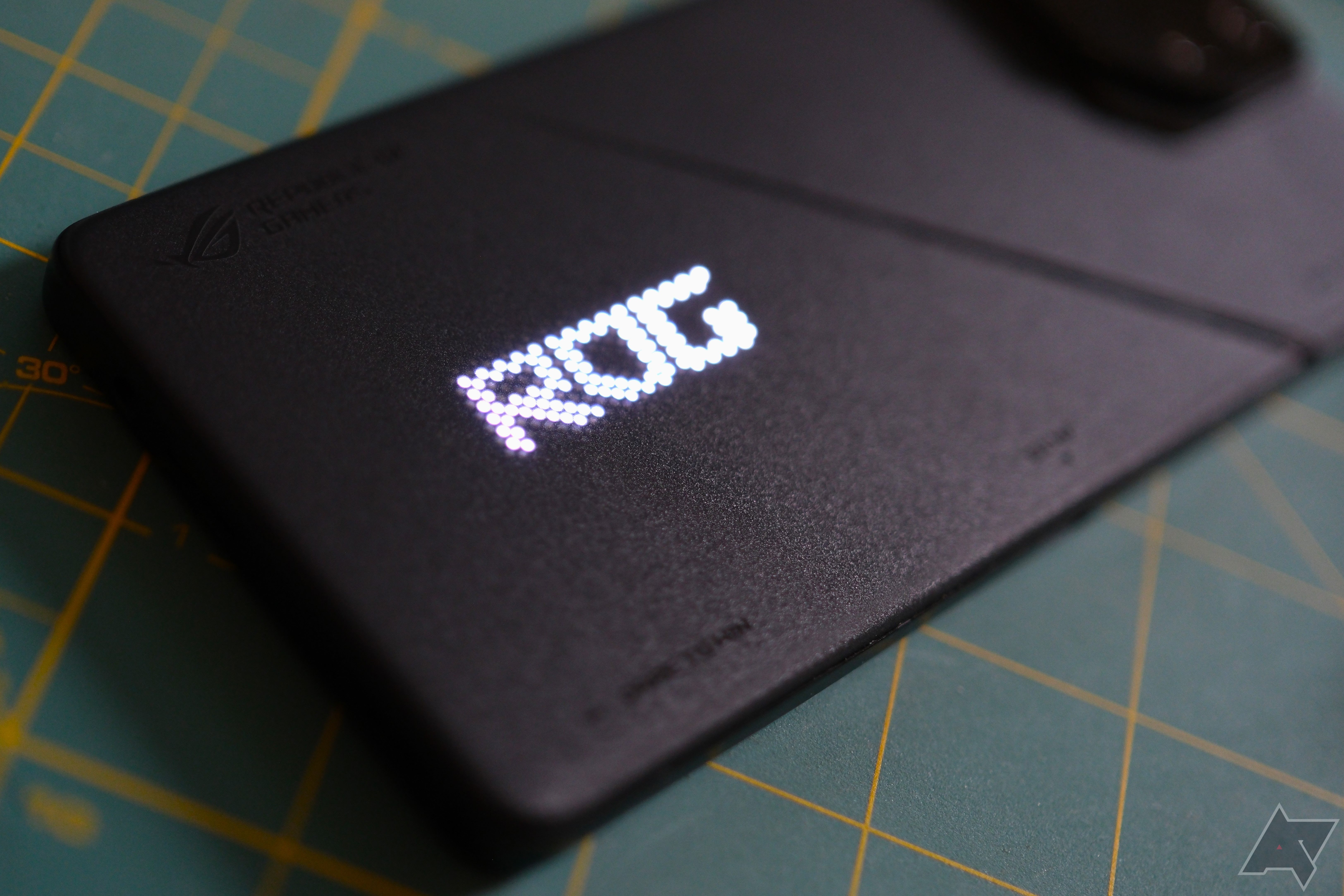 ROG Phone 8 Pro deitado em um tapete de hobby com o logotipo da Rog aparecendo como LEDs brancos