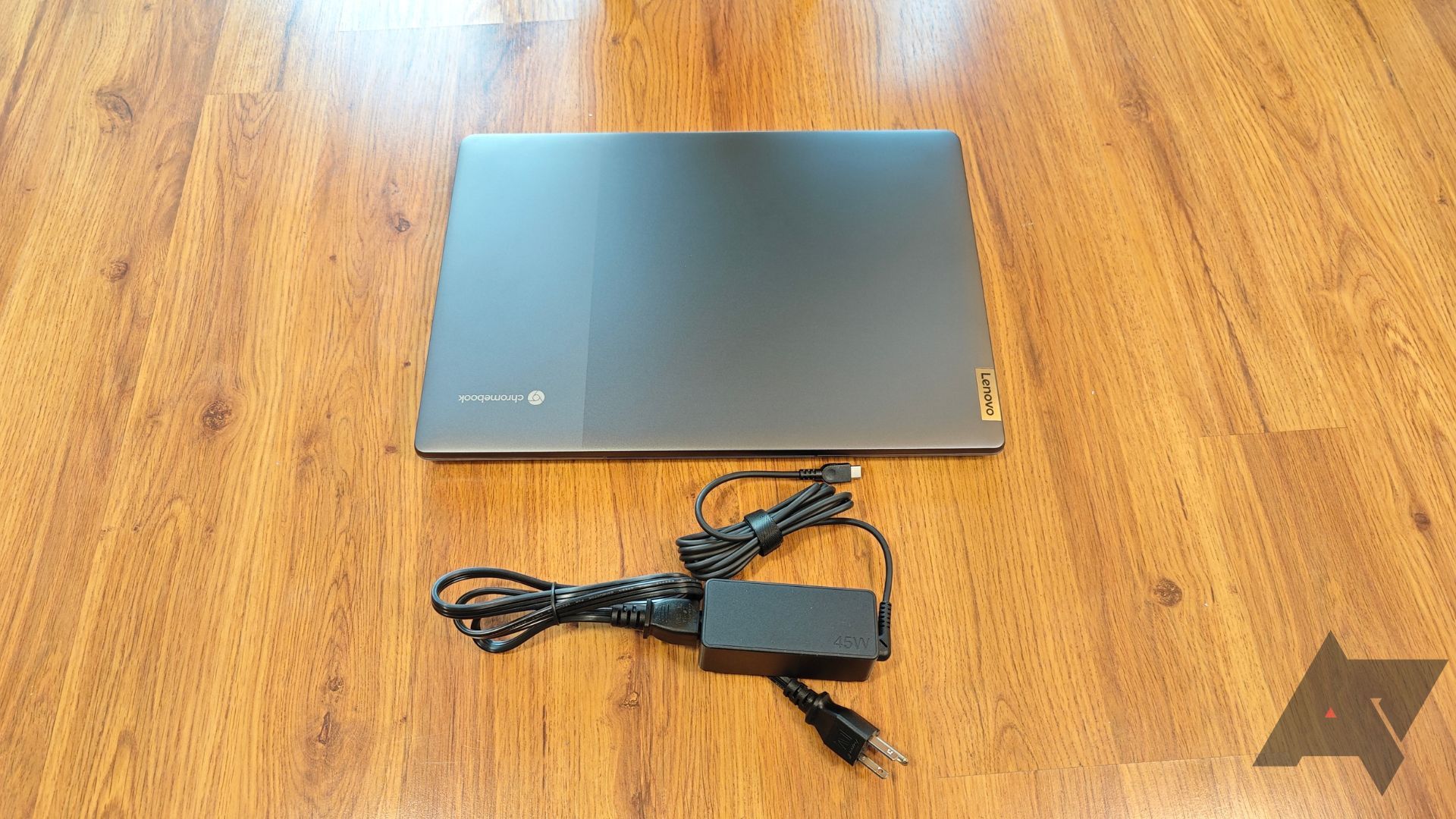 Um Chromebook Lenovo IdeaPad 5i em um piso de madeira com o carregador na frente
