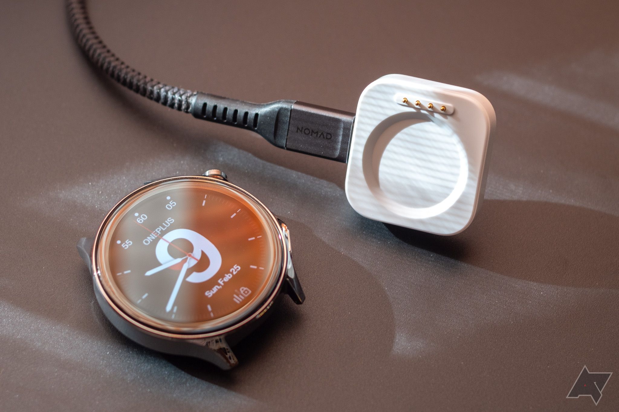 Um smartwatch sem pulseira, próximo ao carregador