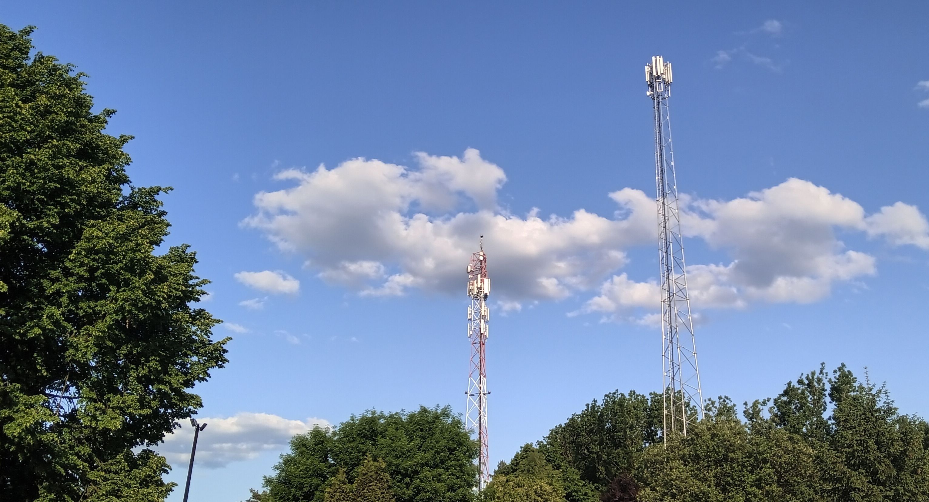 torres de celular ao lado de árvores em frente a um céu azul