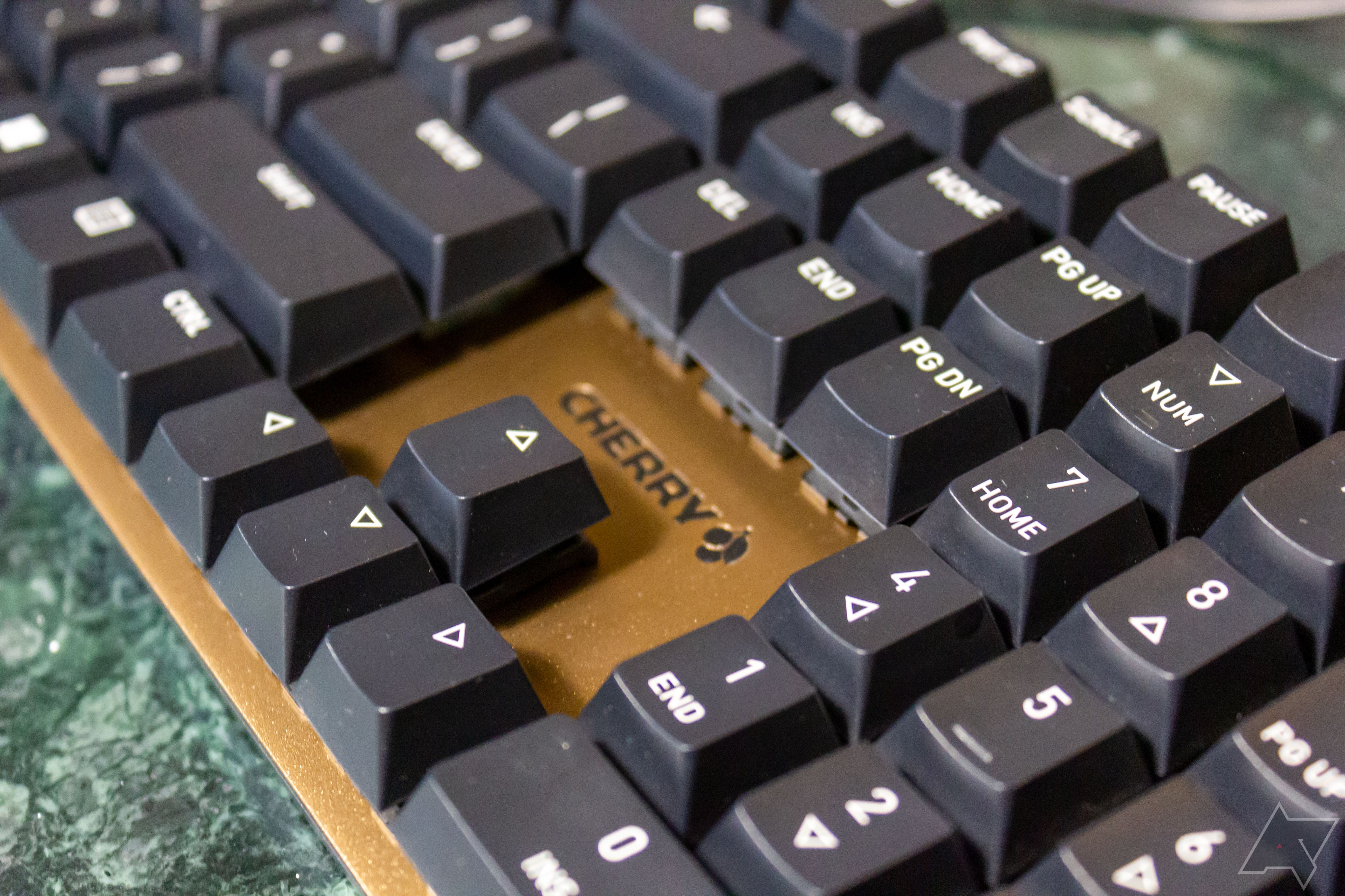 Um teclado preto com uma placa de interruptor marrom-dourada, colocado sobre uma mesa de mármore verde