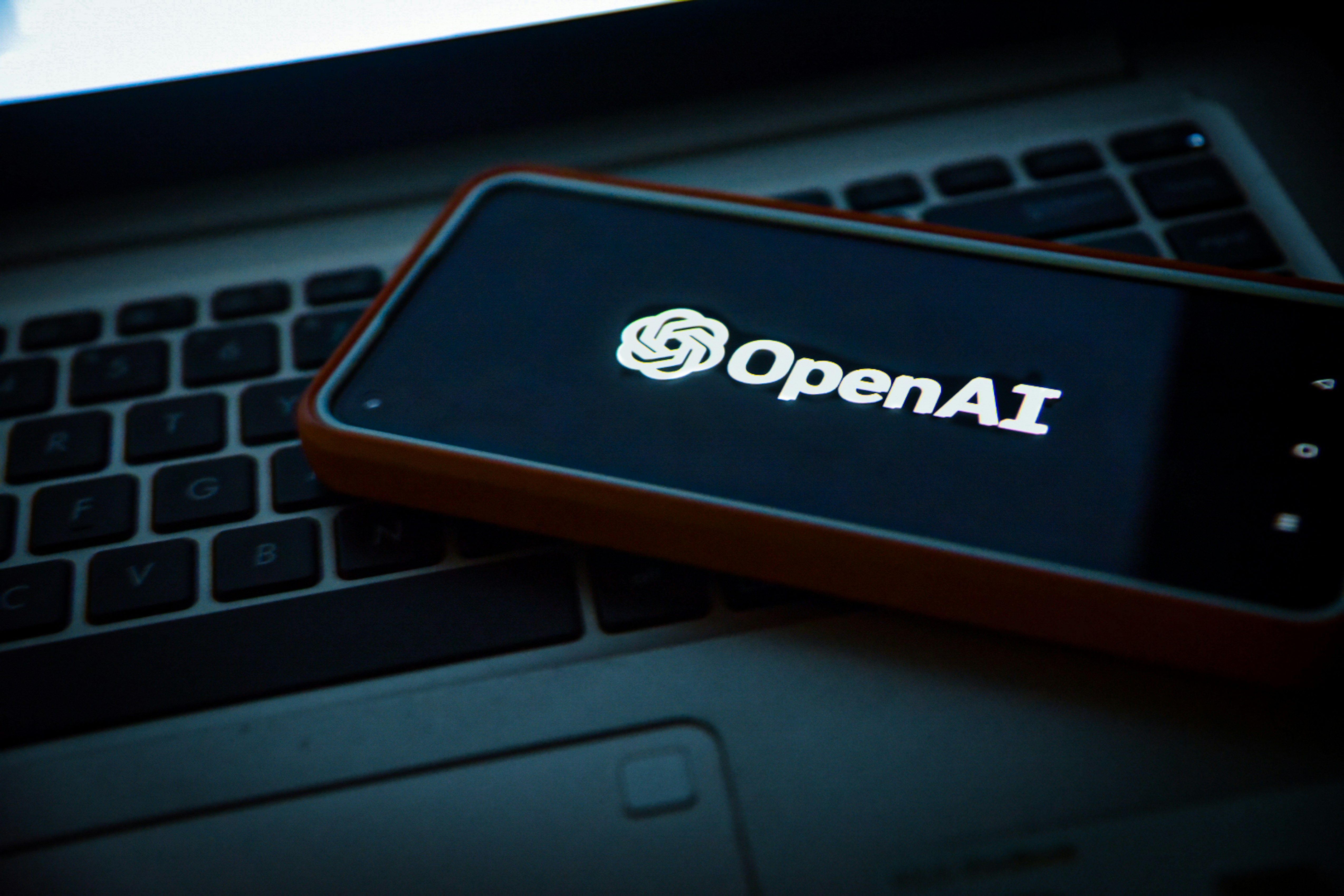 Um smartphone exibindo o logotipo OpenAI em sua tela, colocado no teclado de um laptop.