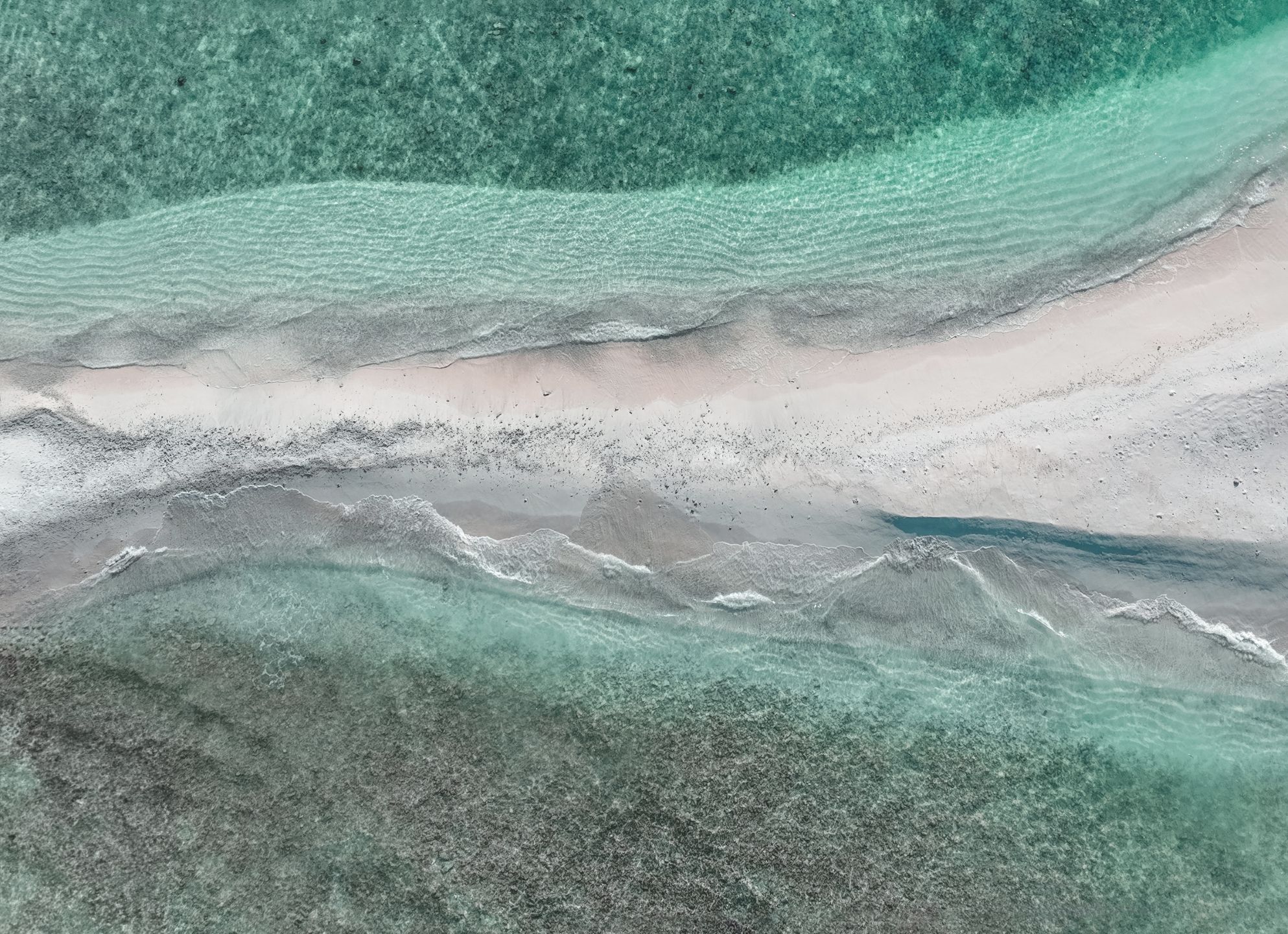 Uma vista aérea das praias de areia branca das Maldivas com águas verdes claras em ambos os lados 