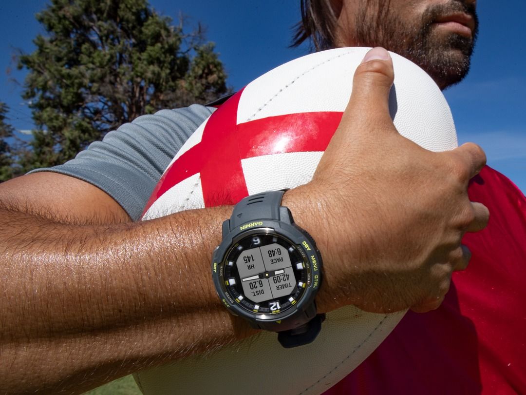 Homem usando um relógio Garmin Forerunner e segurando uma bola de rugby na mão direita.