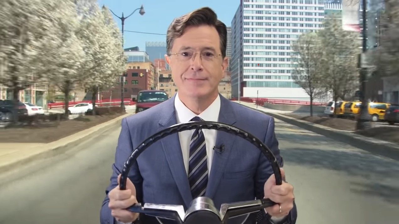 Uma captura de tela de Stephen Colbert dirigindo um carro imaginário pela cidade