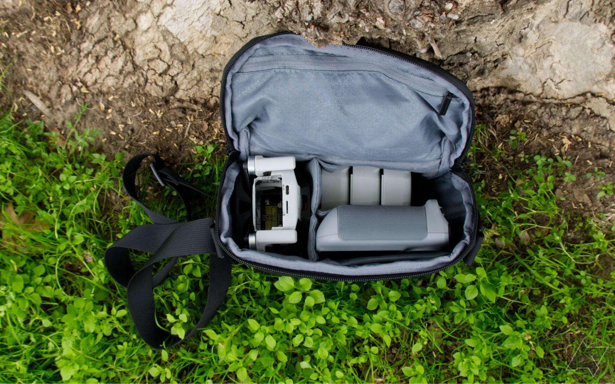 DJI Mini 4 Pro, controlador e baterias dentro da bolsa do kit fly more, encostado em uma árvore e na grama